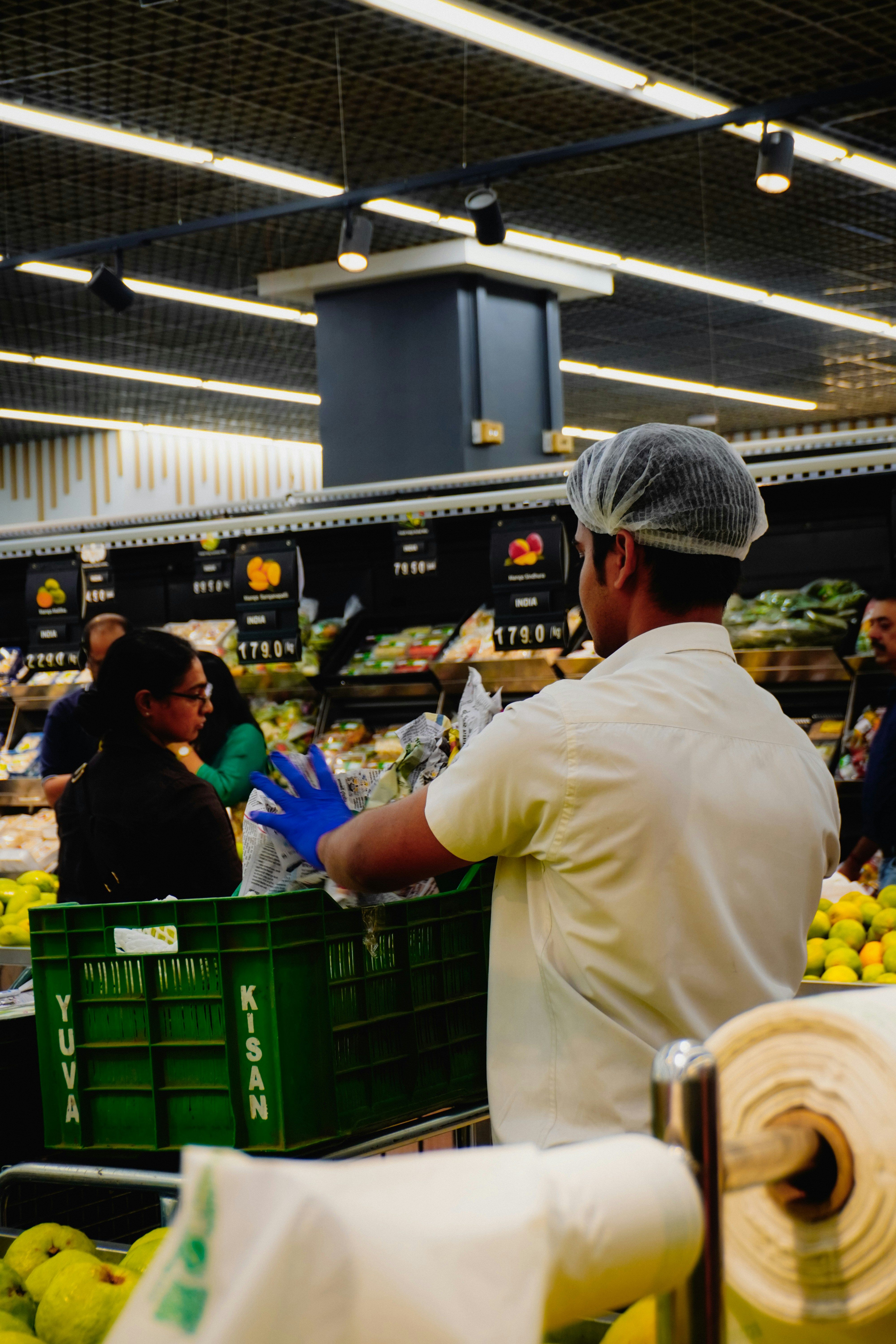 Worker stocking produce in a supermarket aisle.