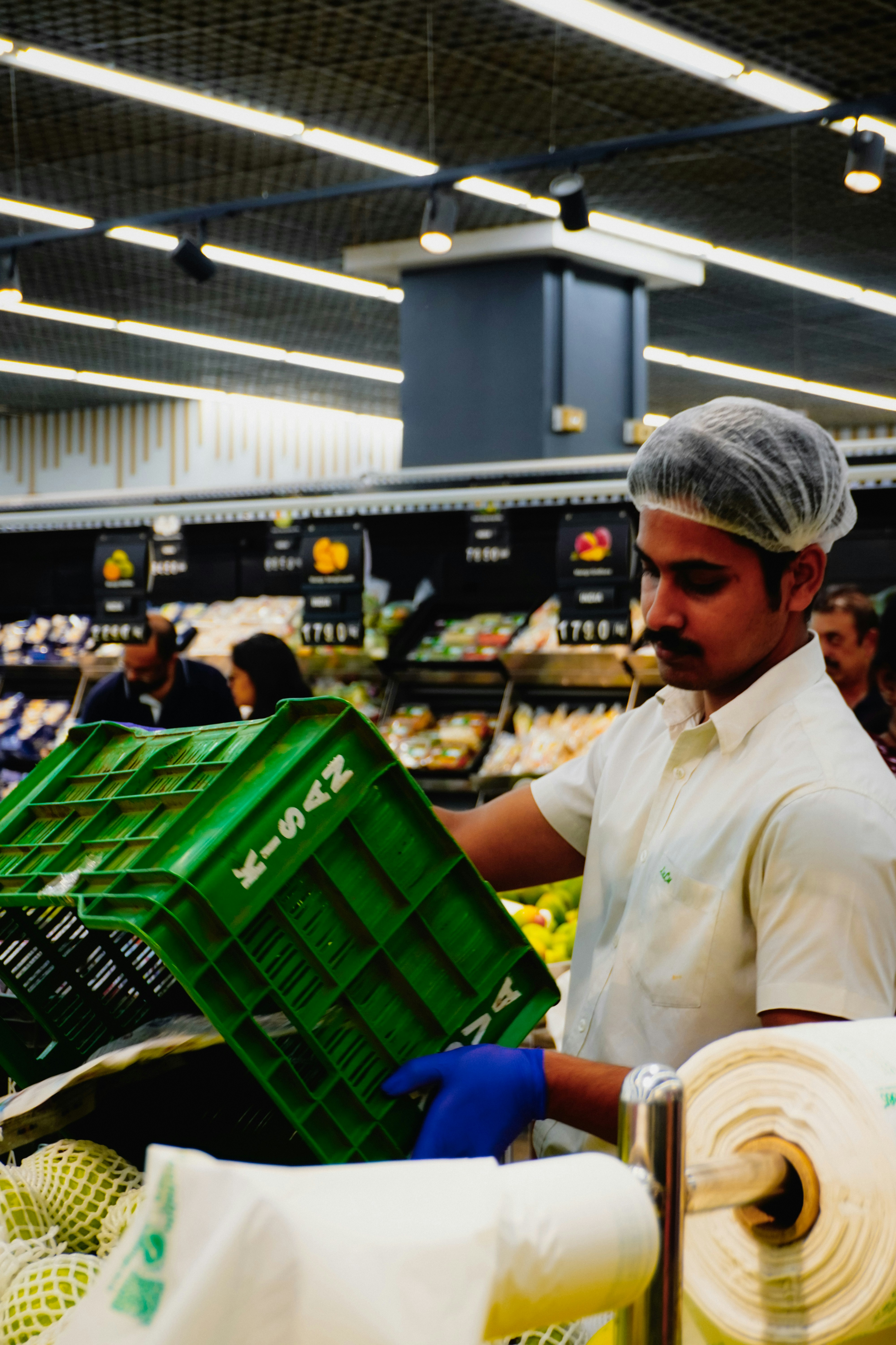 A man in a hairnet stocks produce in a supermarket.
