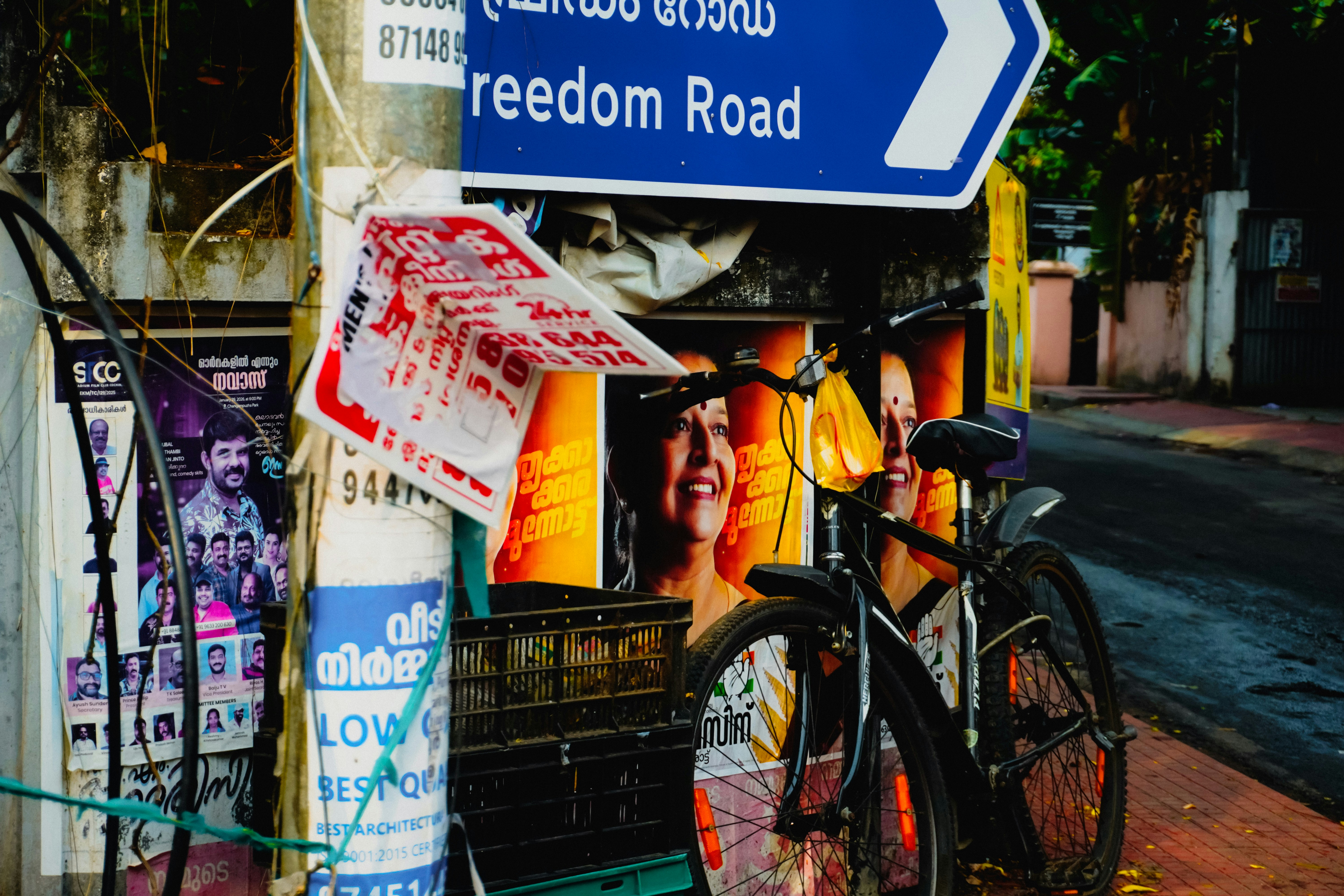 Bicycle parked near a pole with posters and street sign.