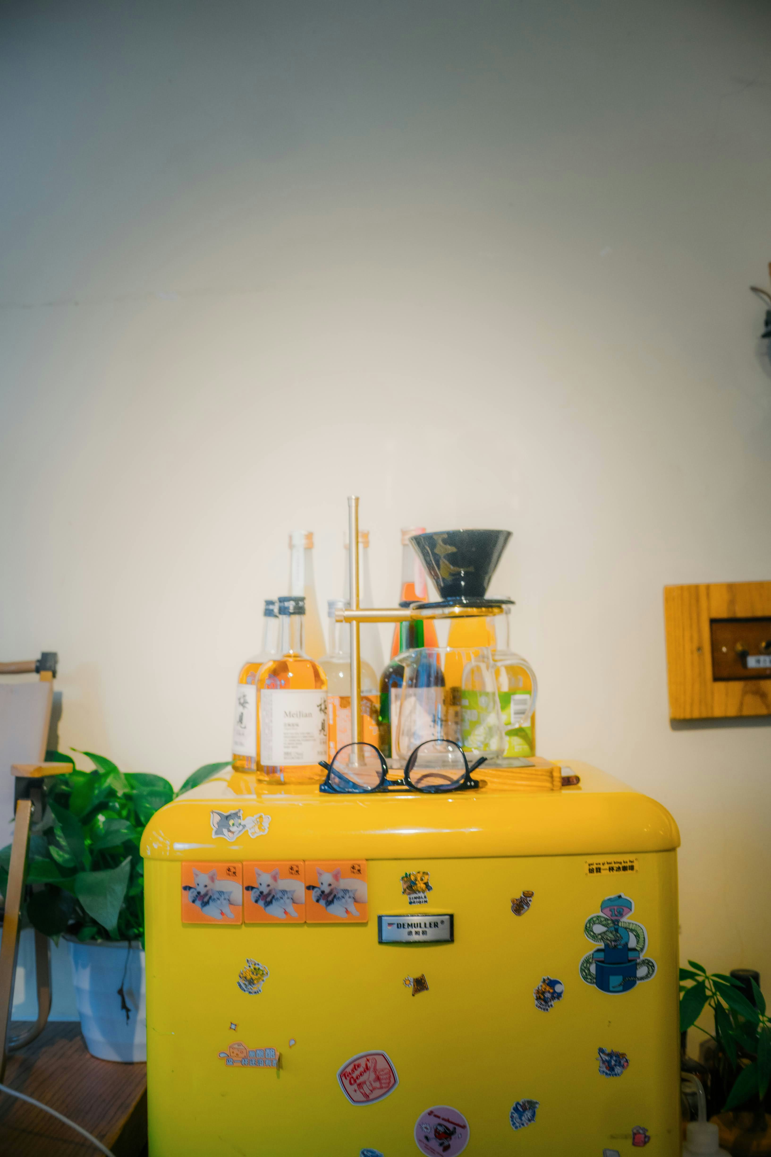 Yellow refrigerator with coffee brewing equipment and bottles.
