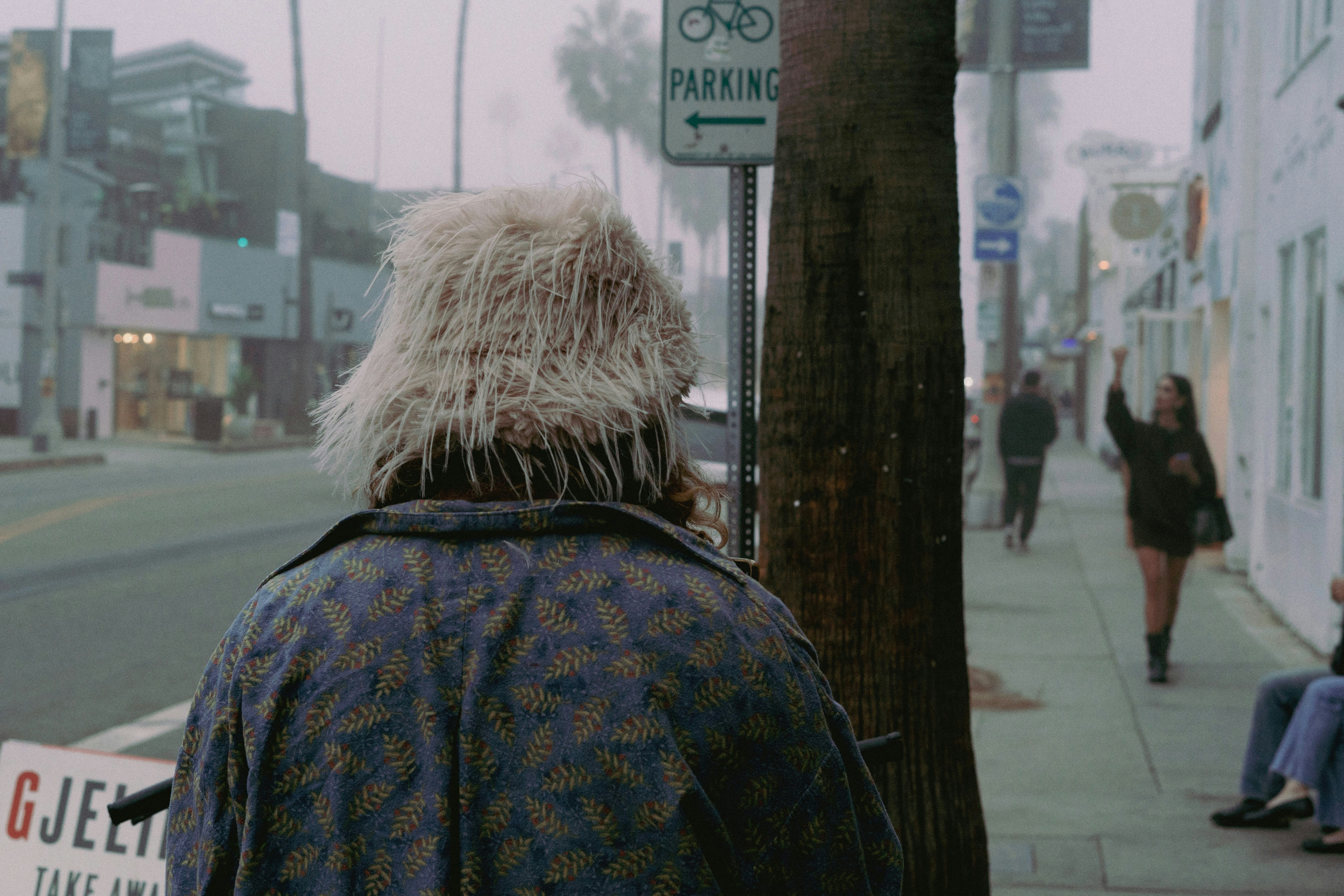 Person with shaggy hair walks down a foggy street.
