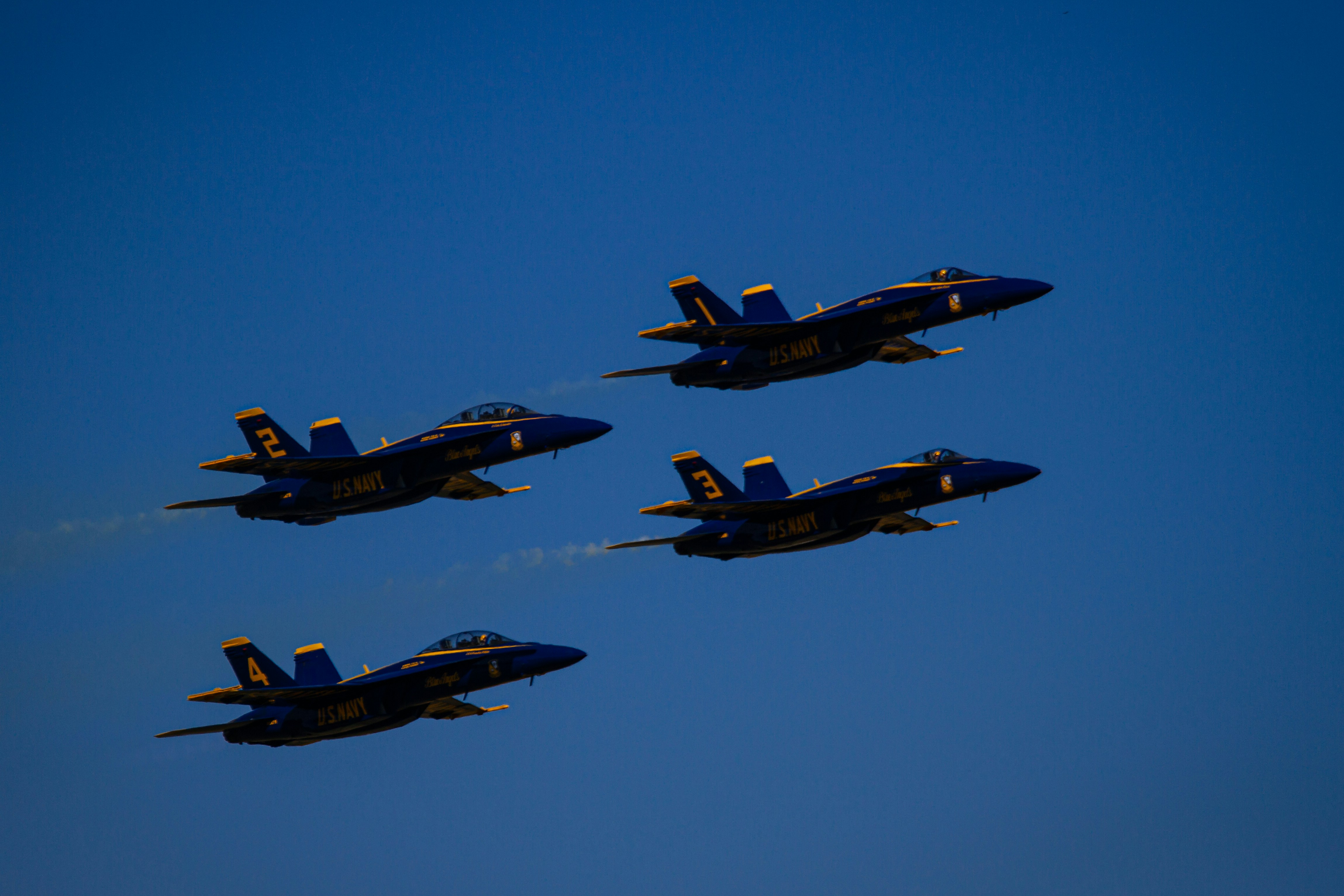 Four blue fighter jets flying in formation against clear sky