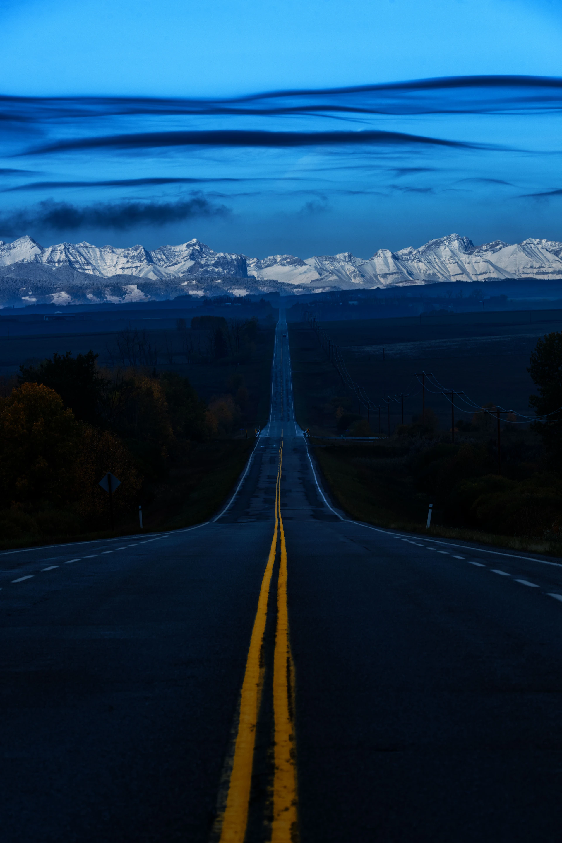 Empty highway leading to snow-capped mountains at dusk