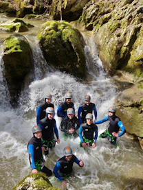 Group wearing wetsuits and helmets in a river with waterfall.