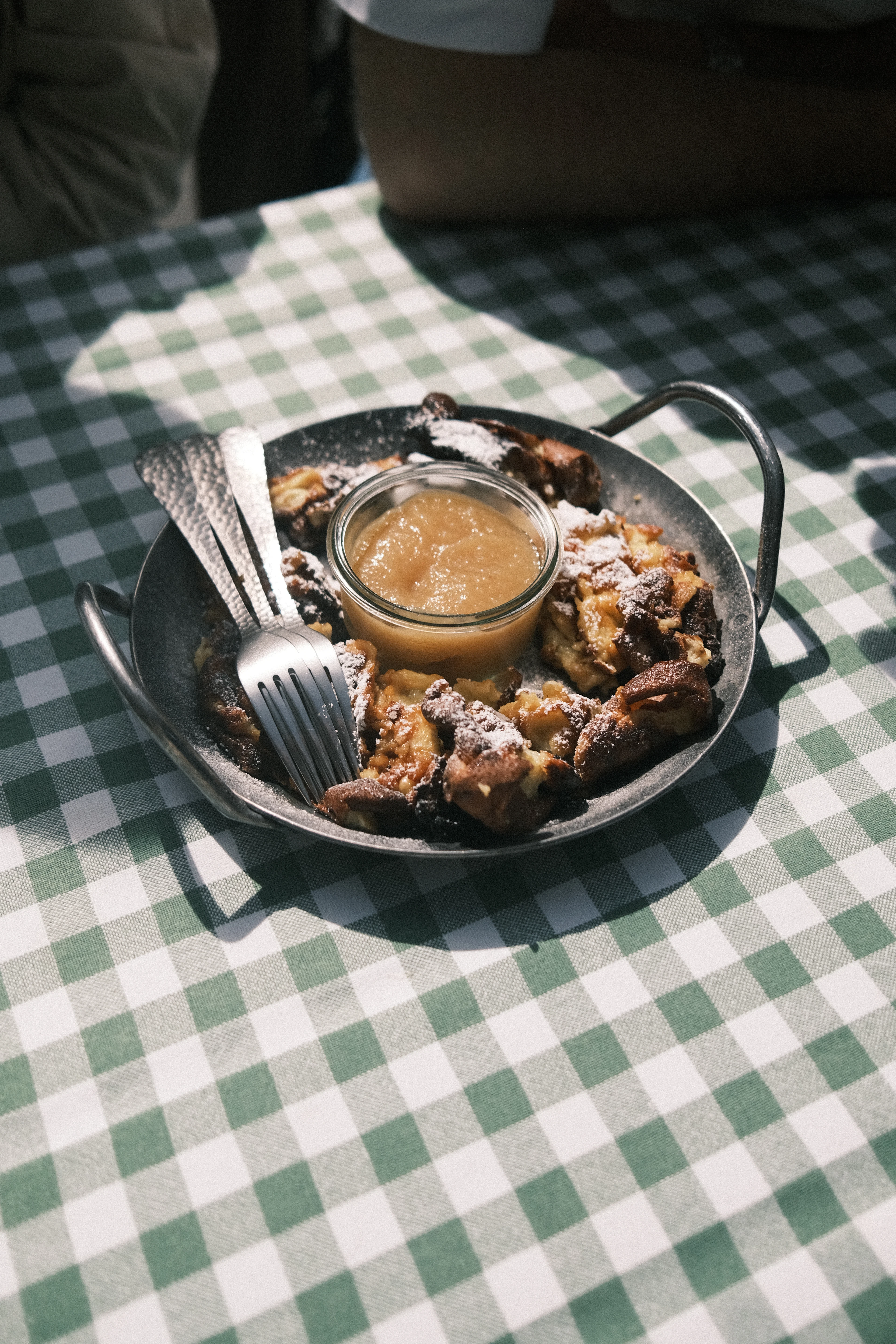 Kaiserschmarrn, the torn and sugar-dusted Austrian pancake, served in its iron pan with a jar of apple sauce on a green checked tavern tablecloth
