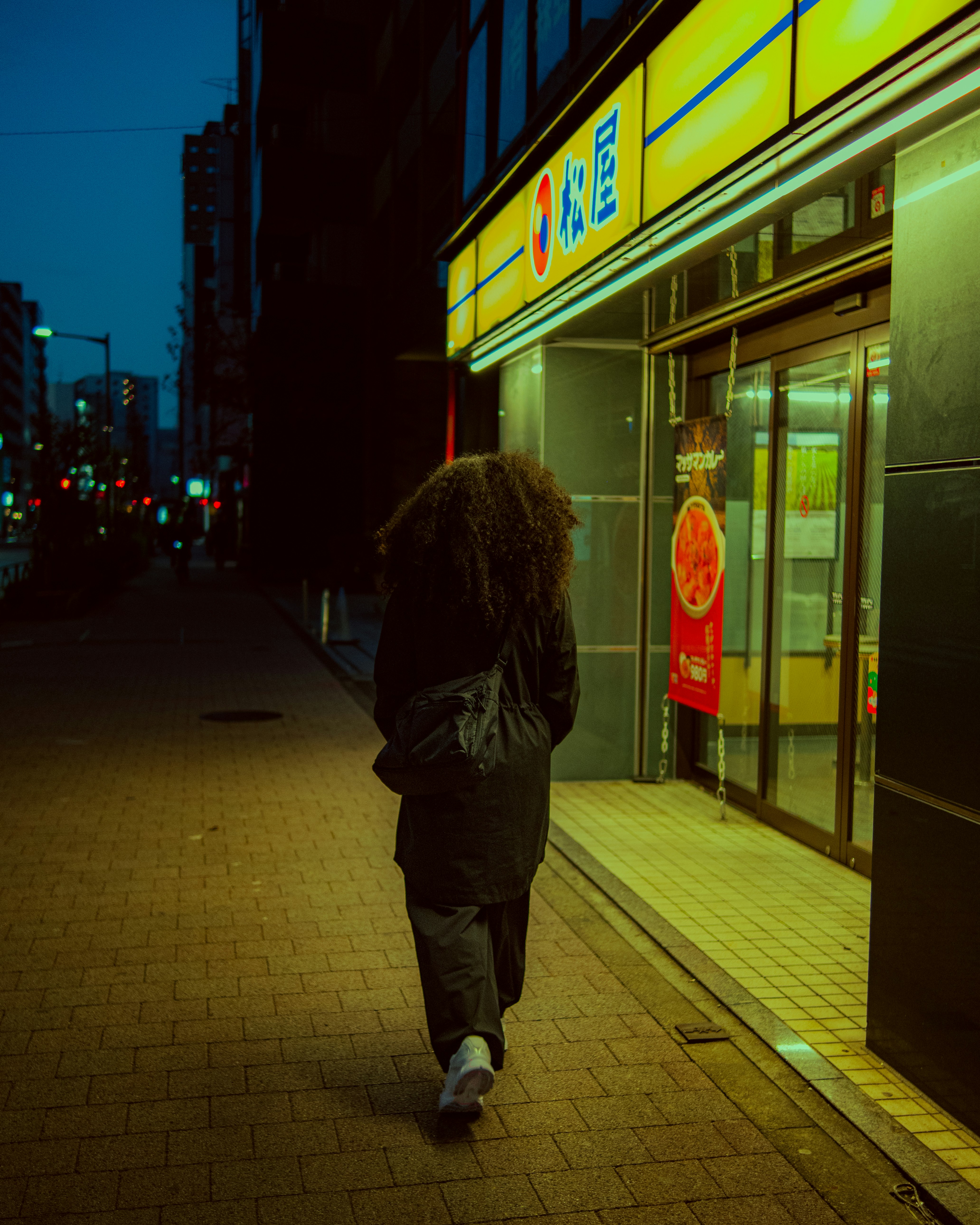 Une personne marche dans une rue la nuit près d’un magasin.