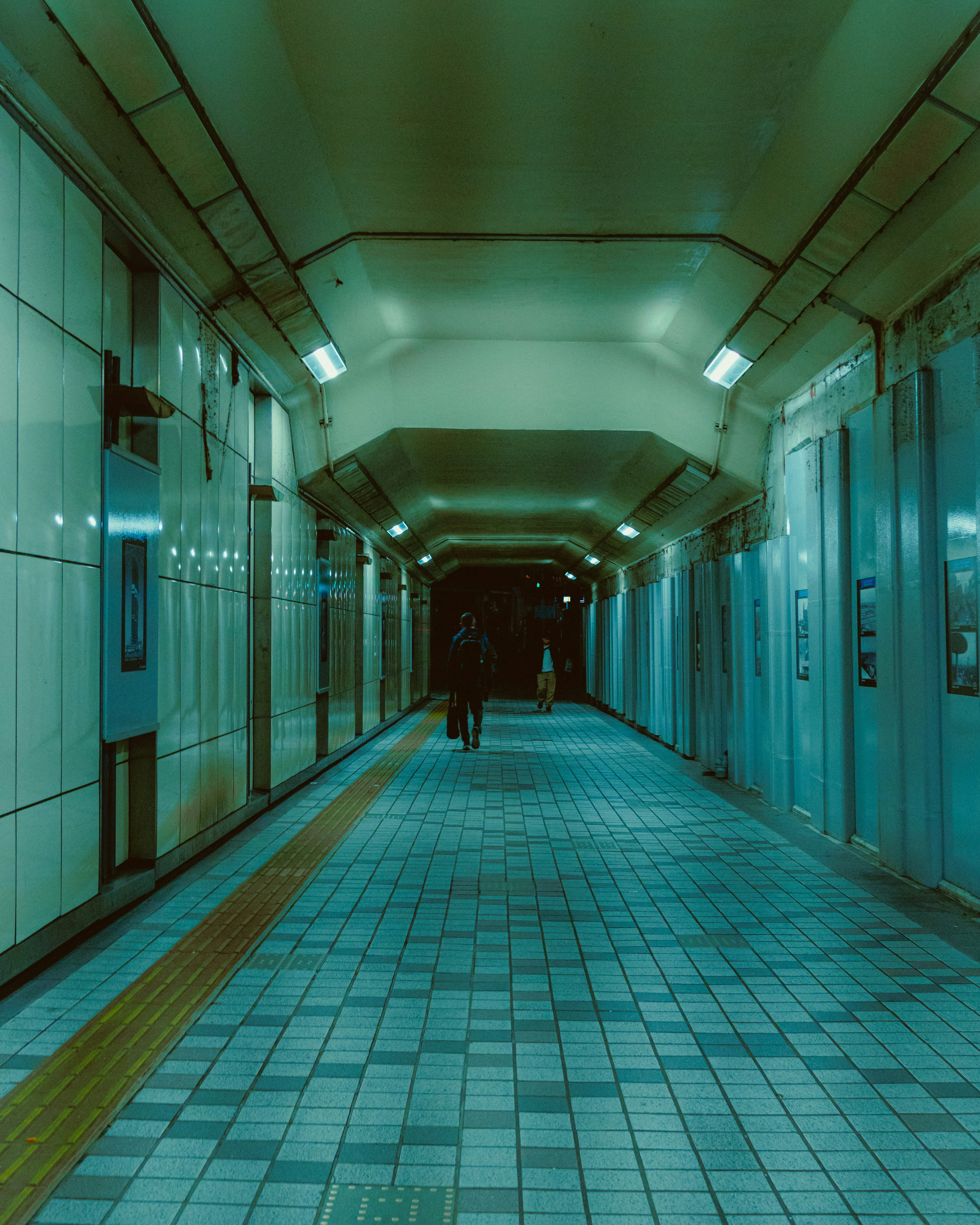 Une silhouette solitaire marche dans un couloir de métro faiblement éclairé.
