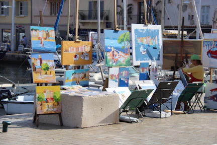 Artist painting by the water with canvases displayed
