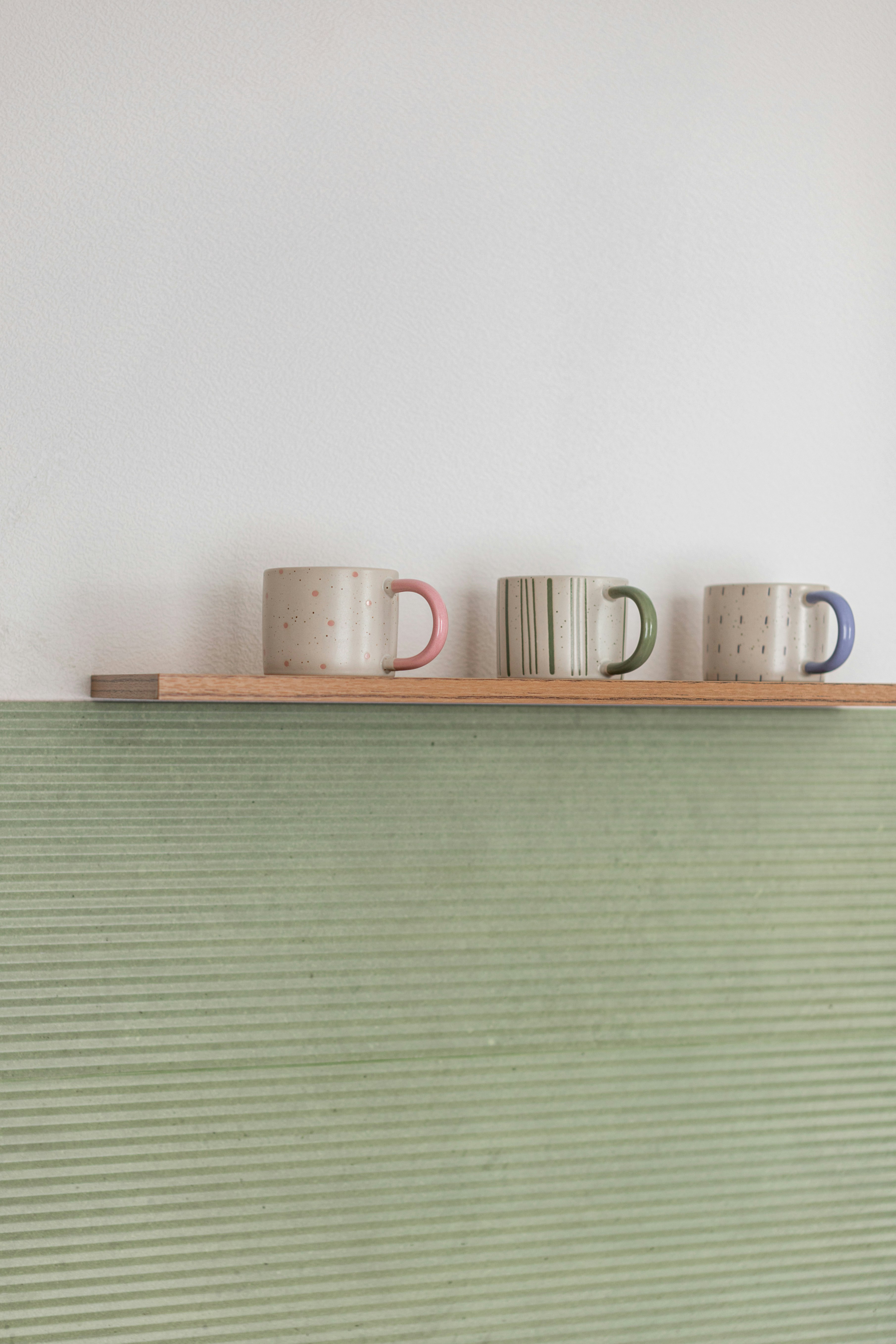 Three decorative mugs sit on a wooden shelf.