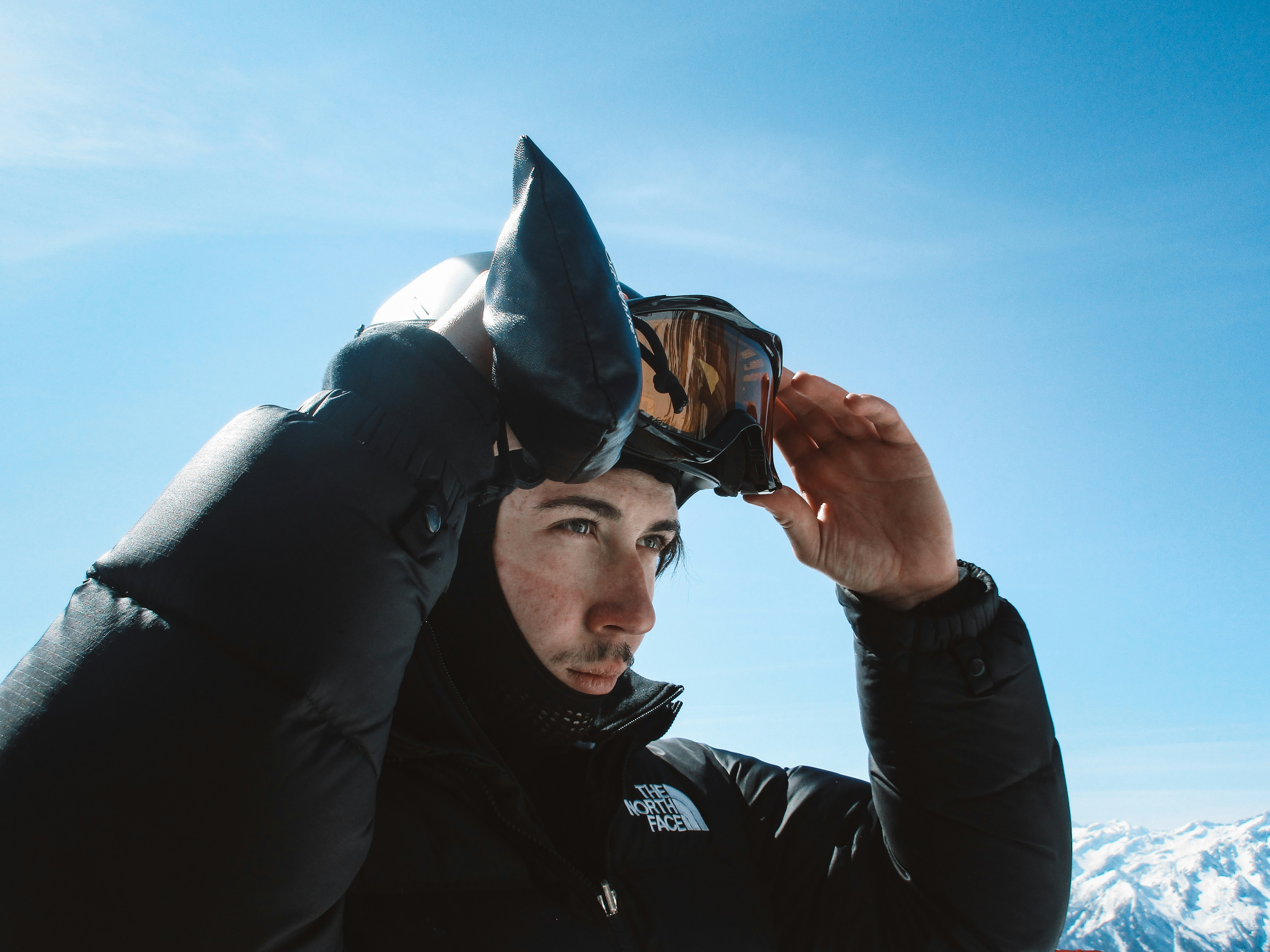 Man adjusting ski goggles on a snowy mountain.