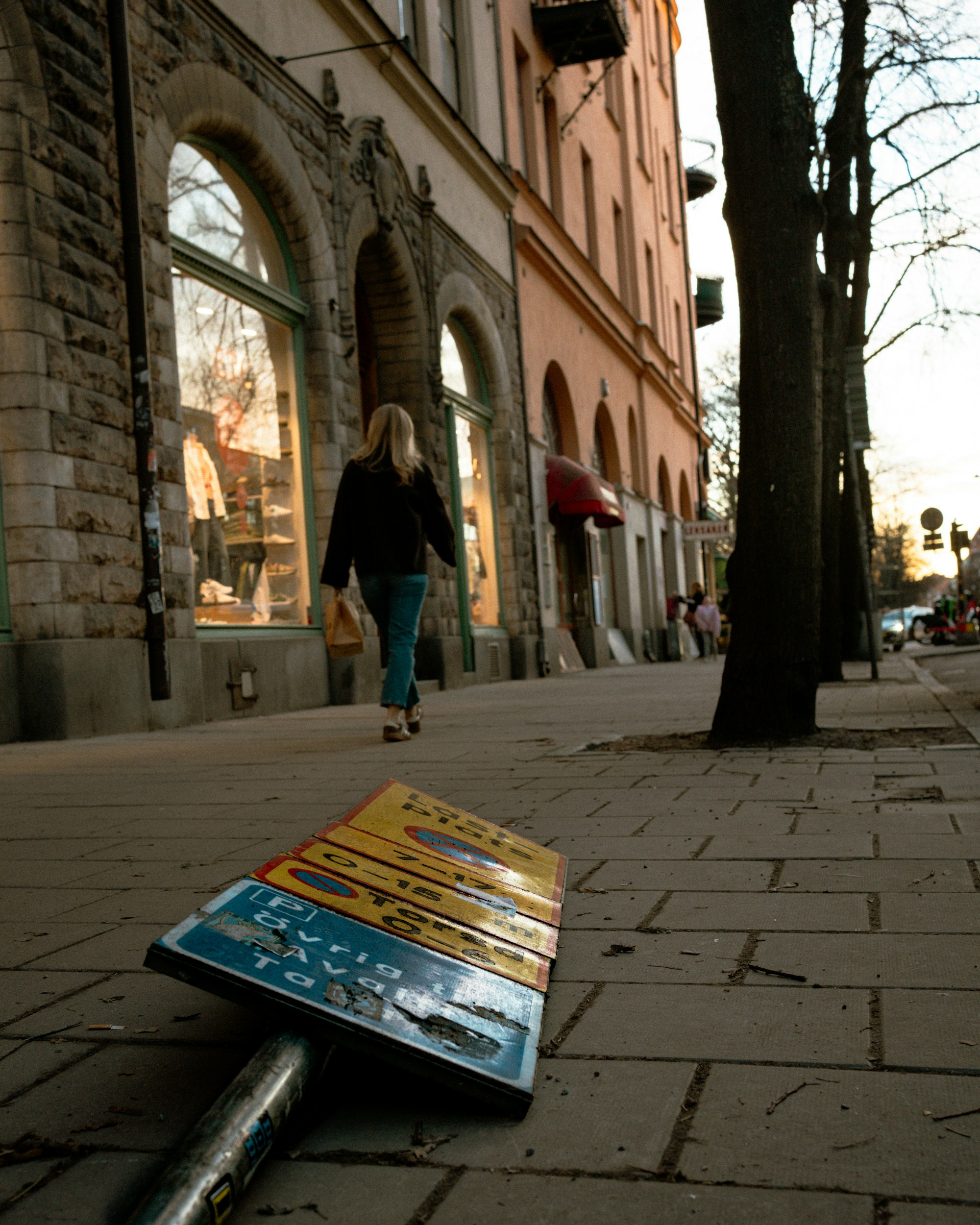A woman walks down a city street past fallen sign.