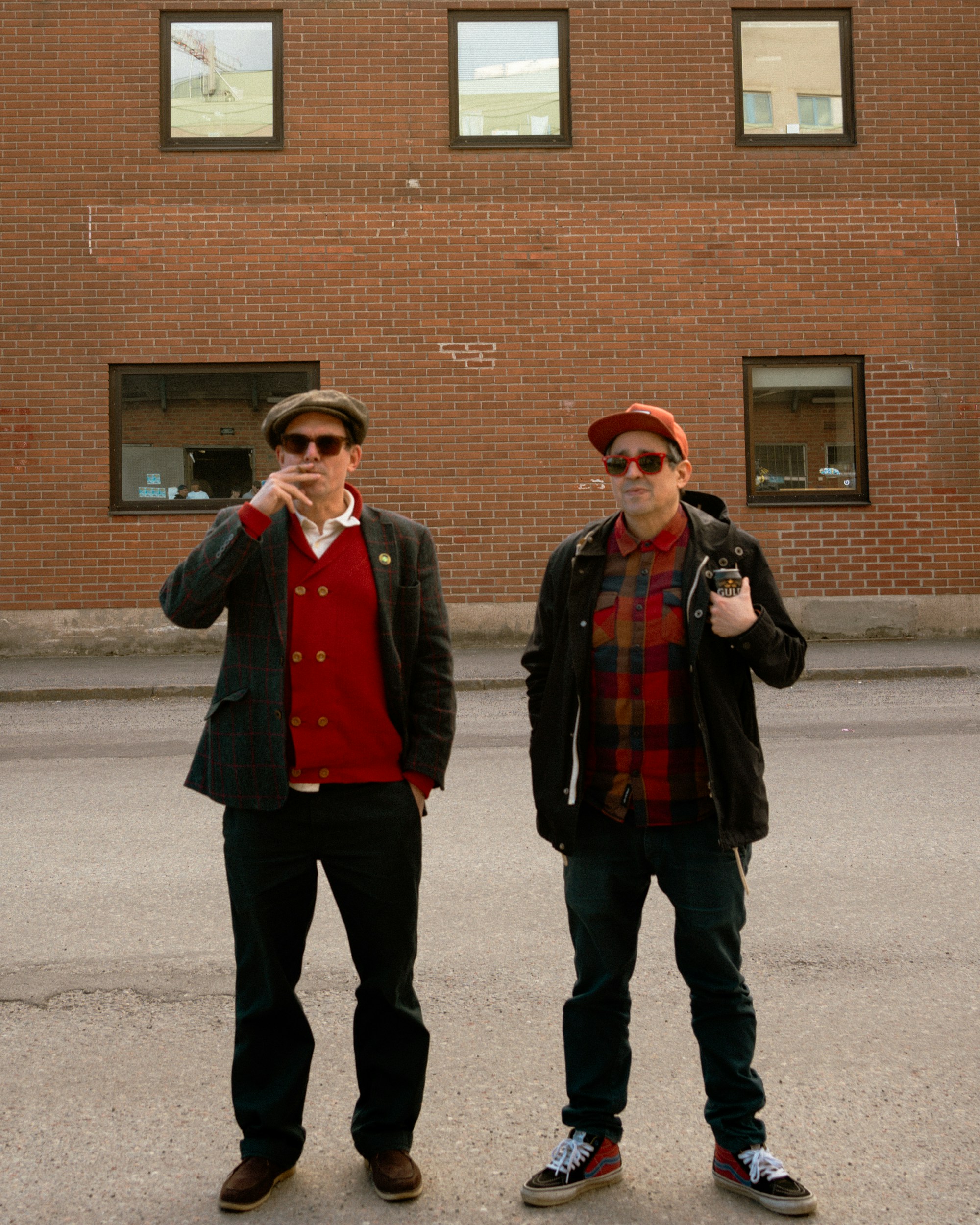 Two men stand in front of a brick building.