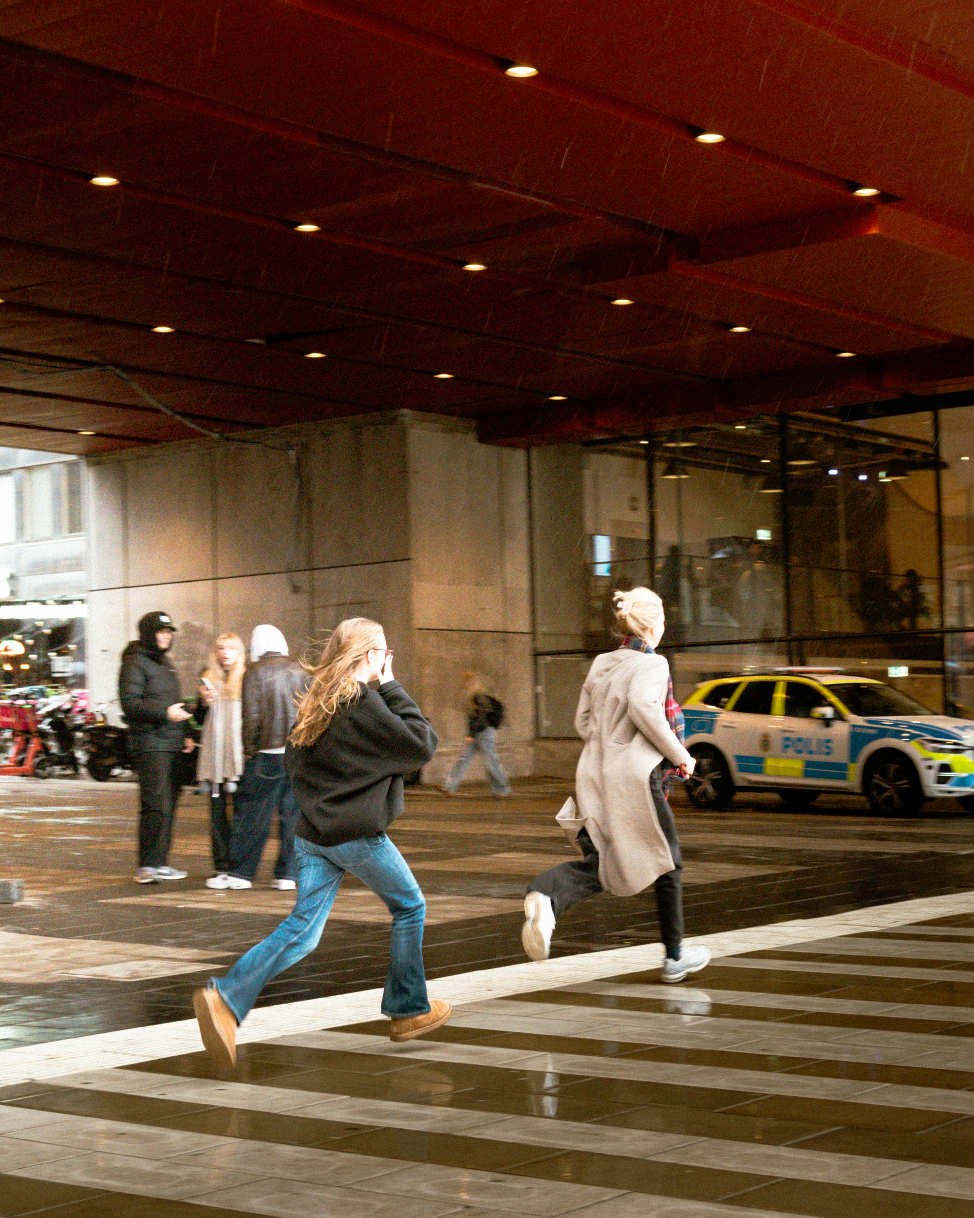 Two women run across a crosswalk with police car nearby.
