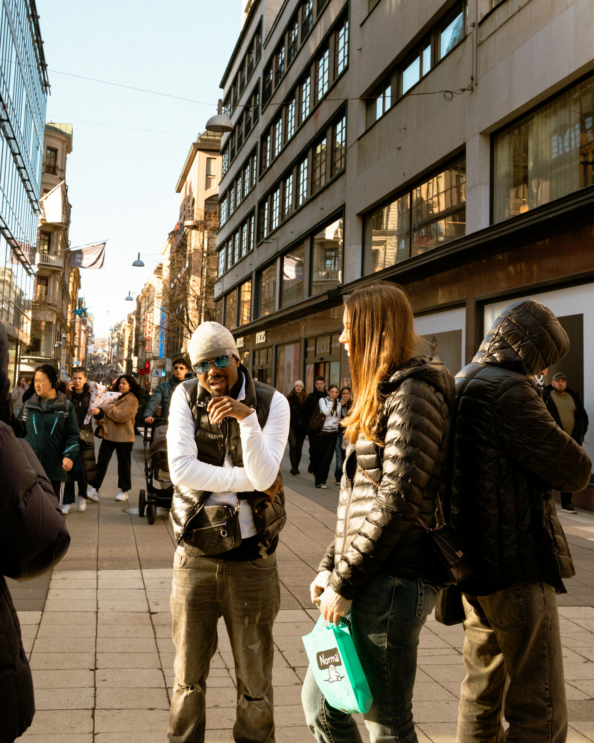 People walking on a sunny city street with buildings.