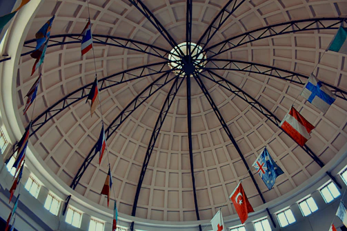 Flags of various nations hang inside a domed building.