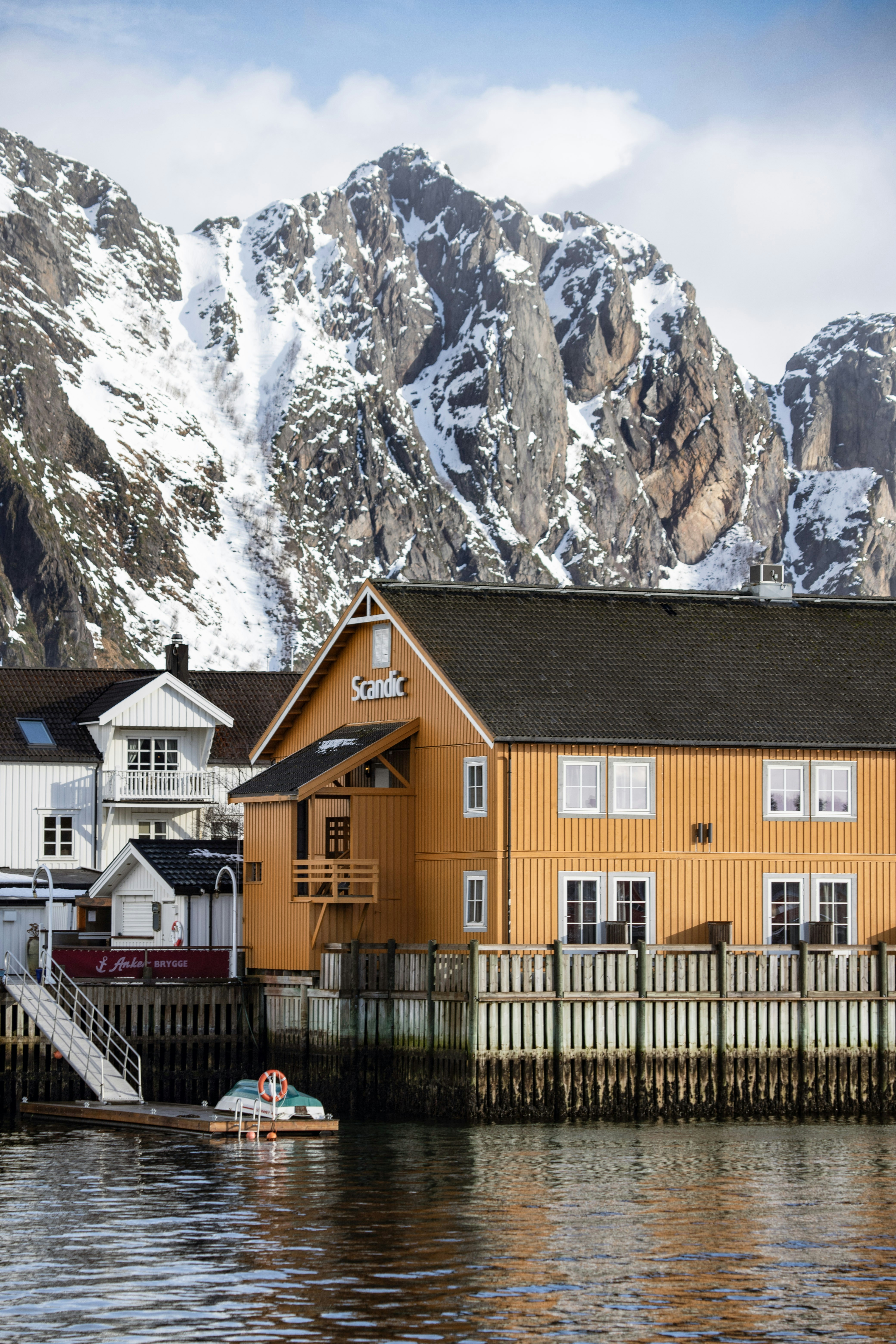 Edificios coloridos en un paseo marítimo con montañas nevadas.