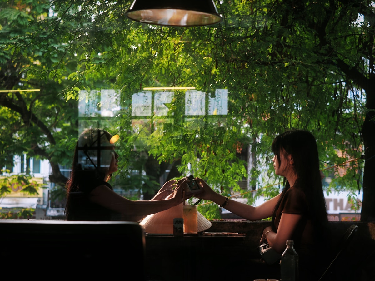 Two women toasting drinks through a window.
