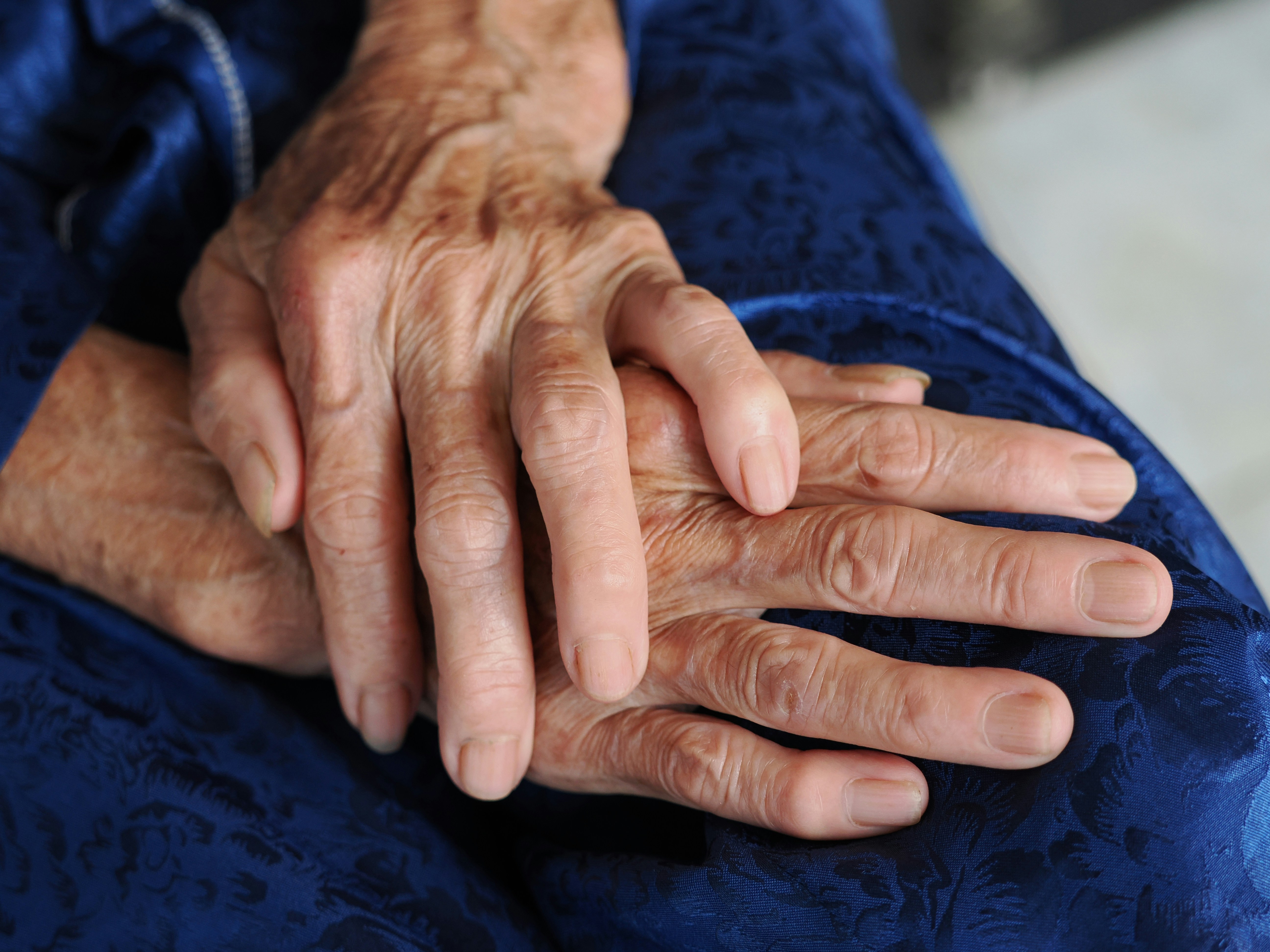 Primer plano de manos ancianas descansando sobre una tela azul.