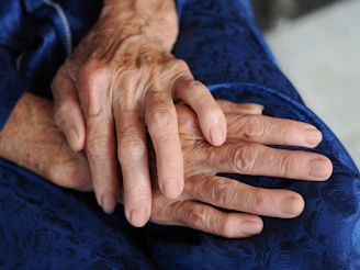 Close-up of elderly hands resting on a blue fabric.
