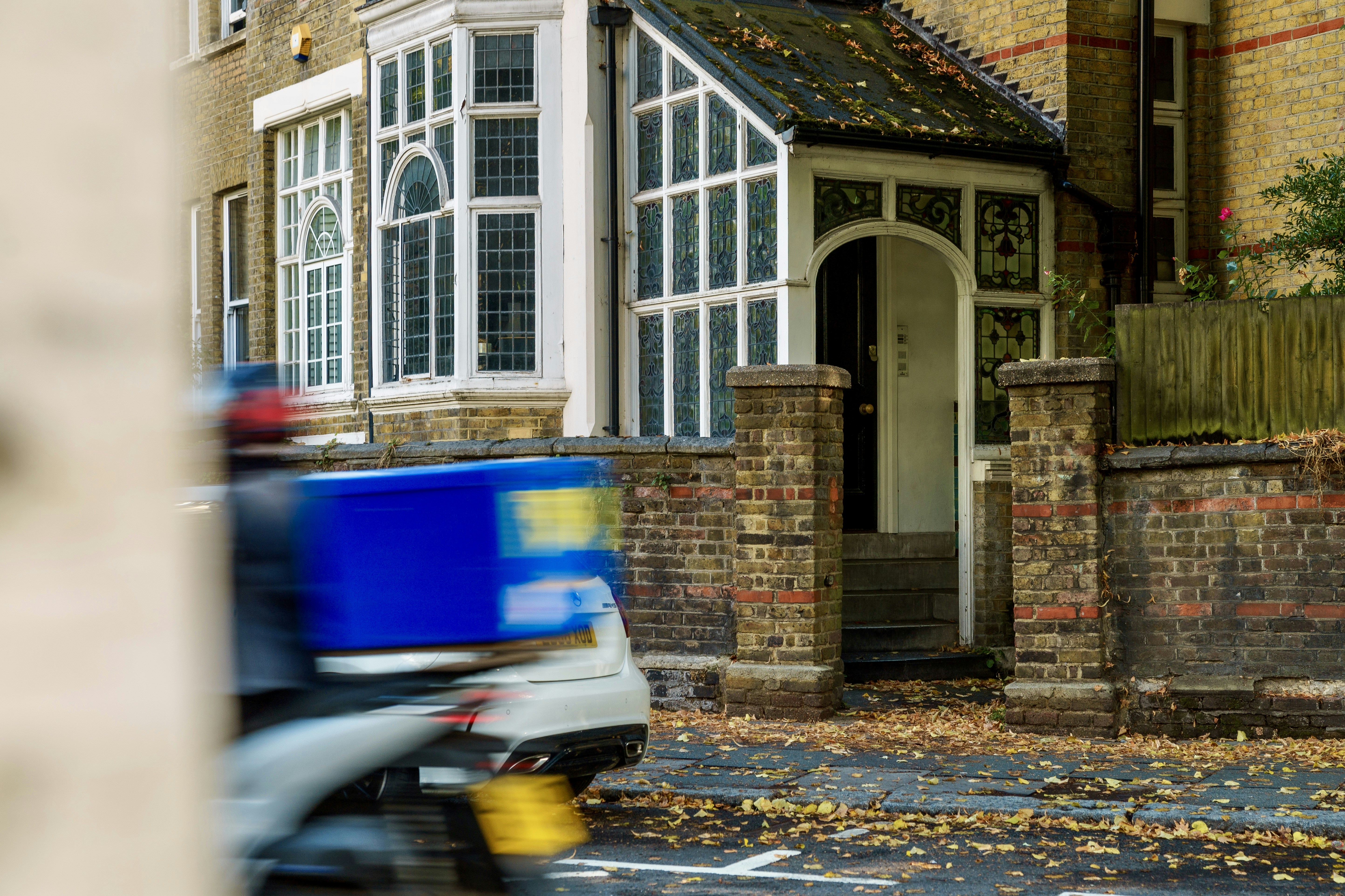 Delivery scooter with blue box passes brick house