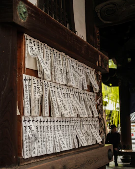 Many japanese prayer slips hang on a wooden structure.