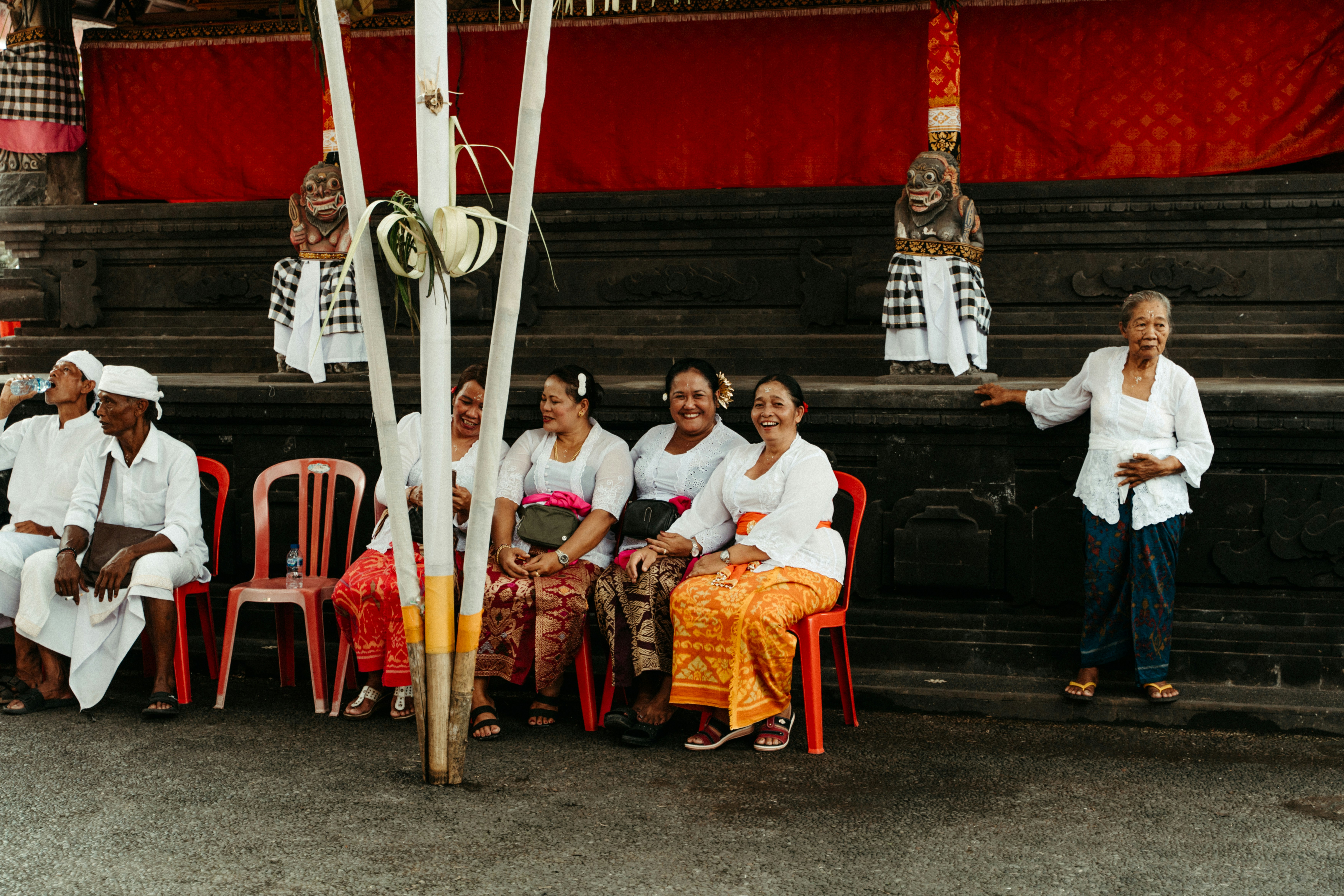 Group of people sitting and standing near a red backdrop.