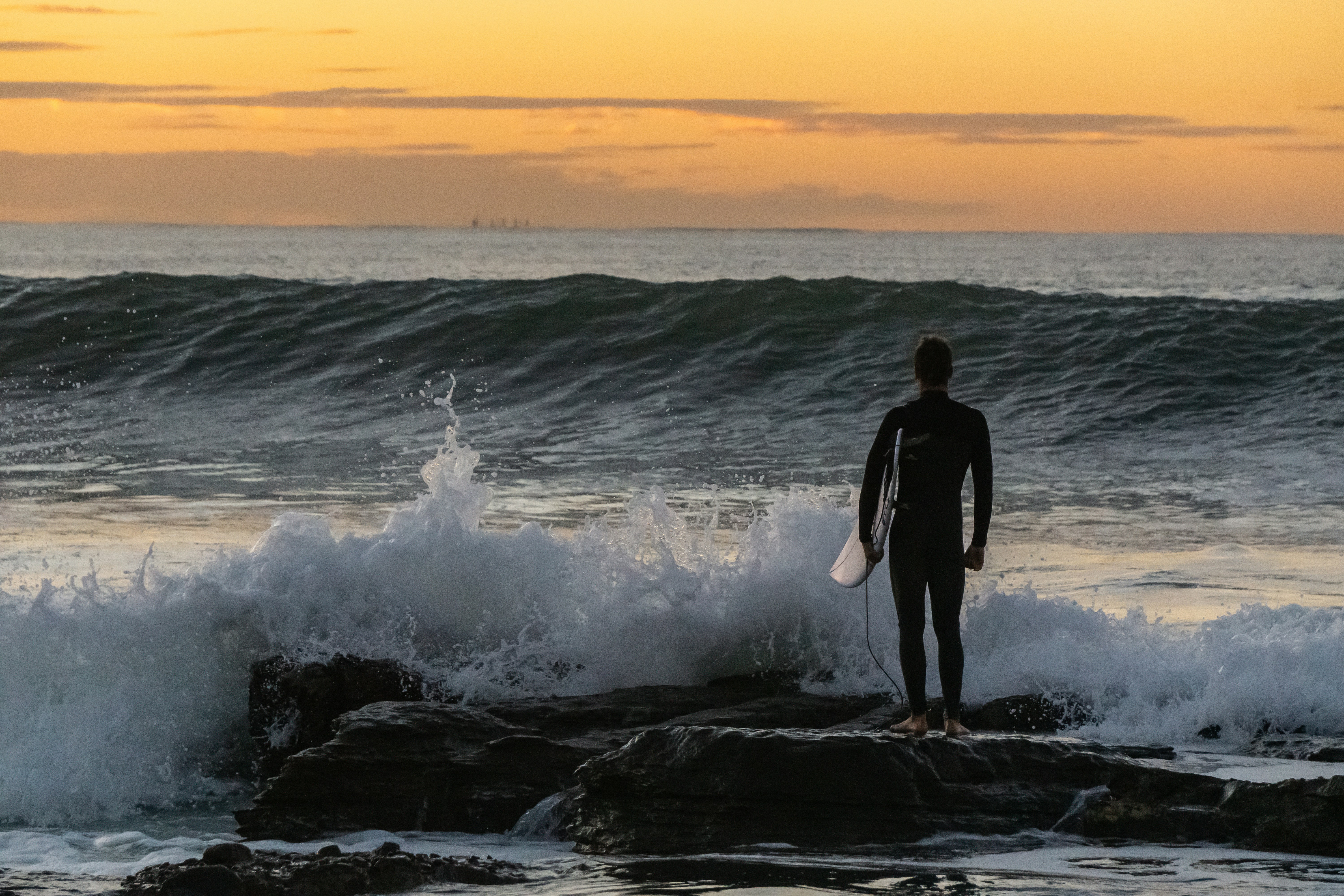 Surfer in wetsuit stands on rocks by ocean waves