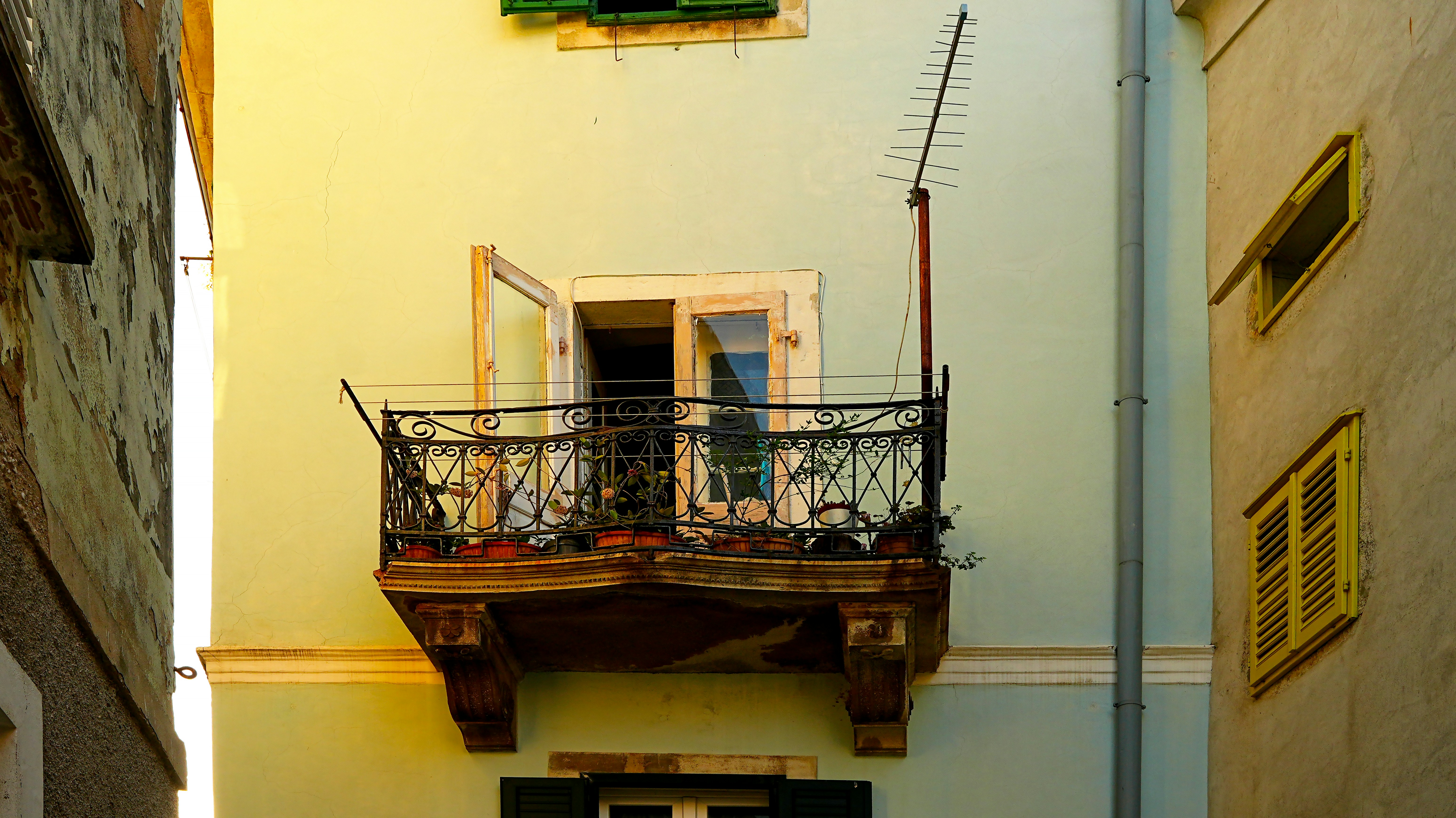 Un balcon sur un bâtiment vert clair aux fenêtres jaunes.
