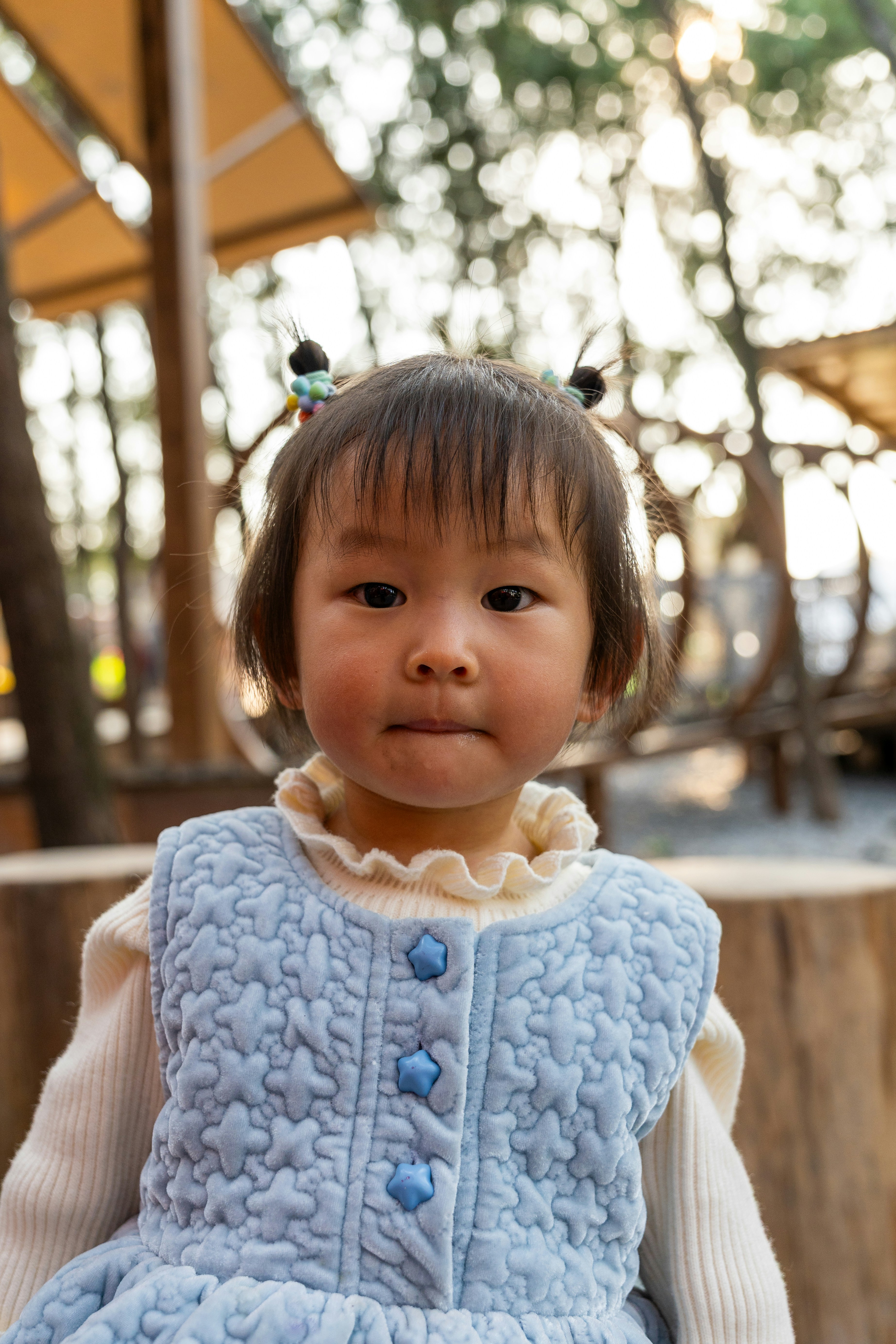 Ein kleines Kind mit Zöpfen, das eine blaue Weste trägt.