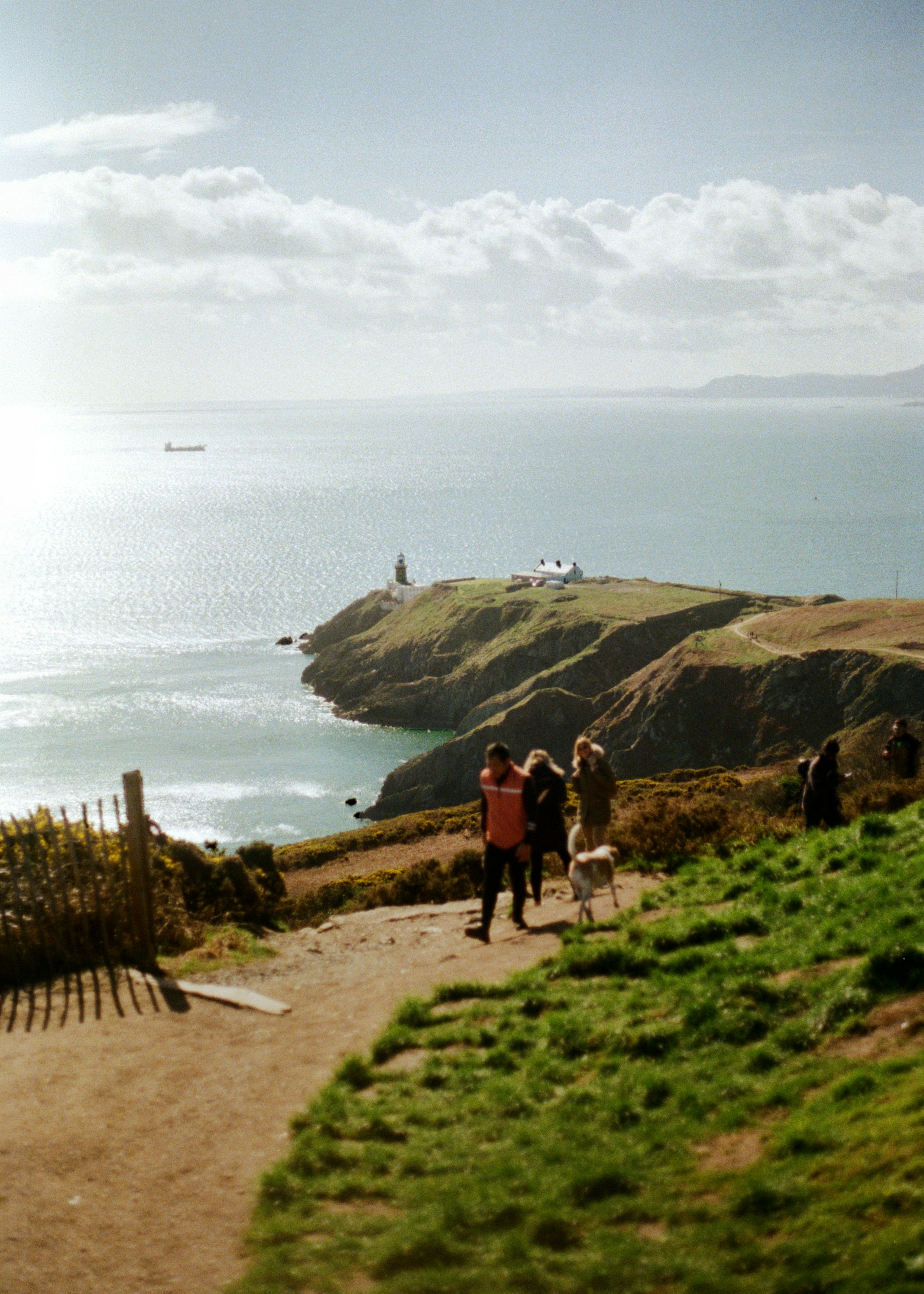People walking on a coastal path with lighthouse ahead