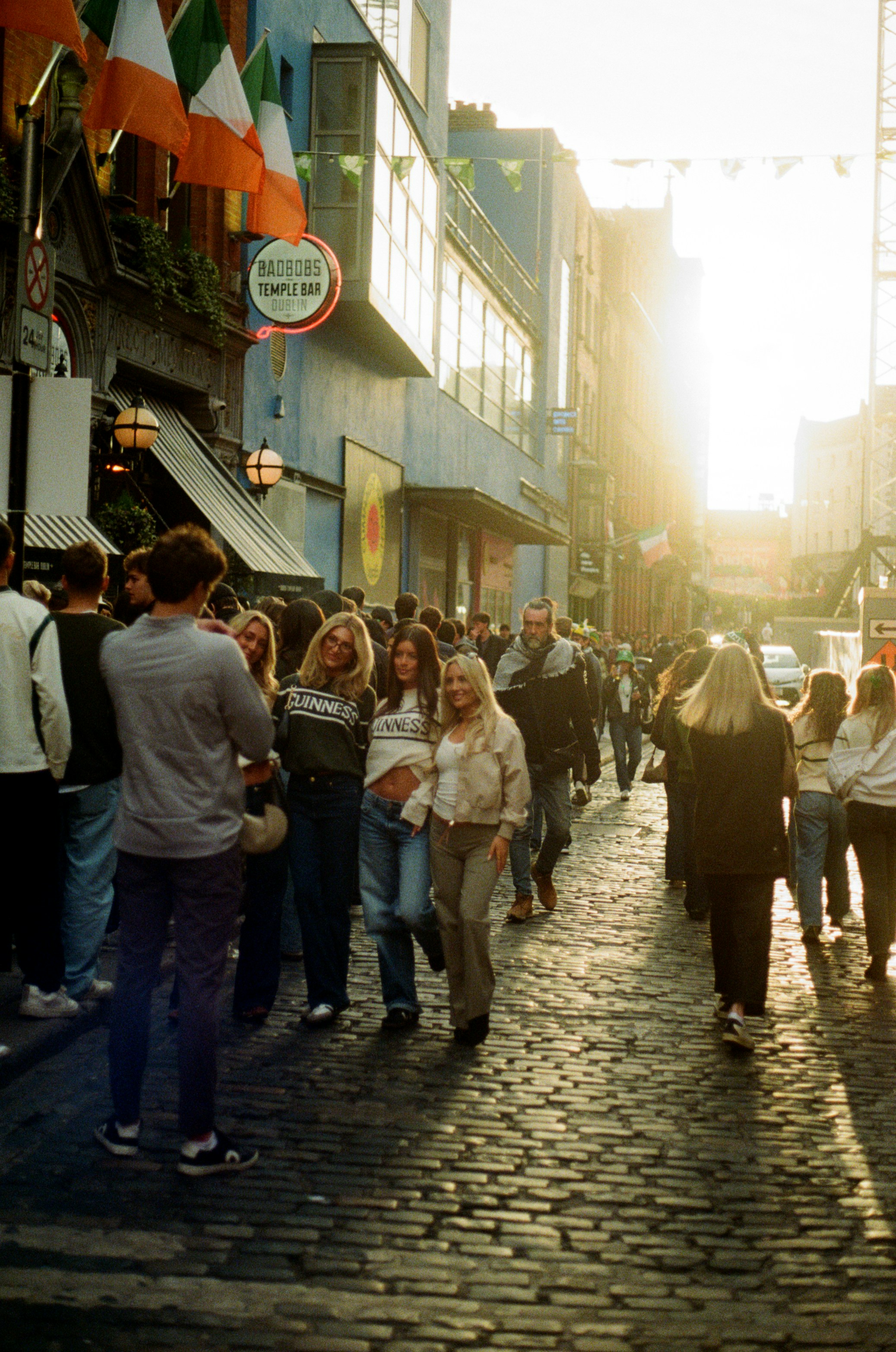 Menschen, die eine Kopfsteinpflasterstraße mit irischen Flaggen entlanggehen.