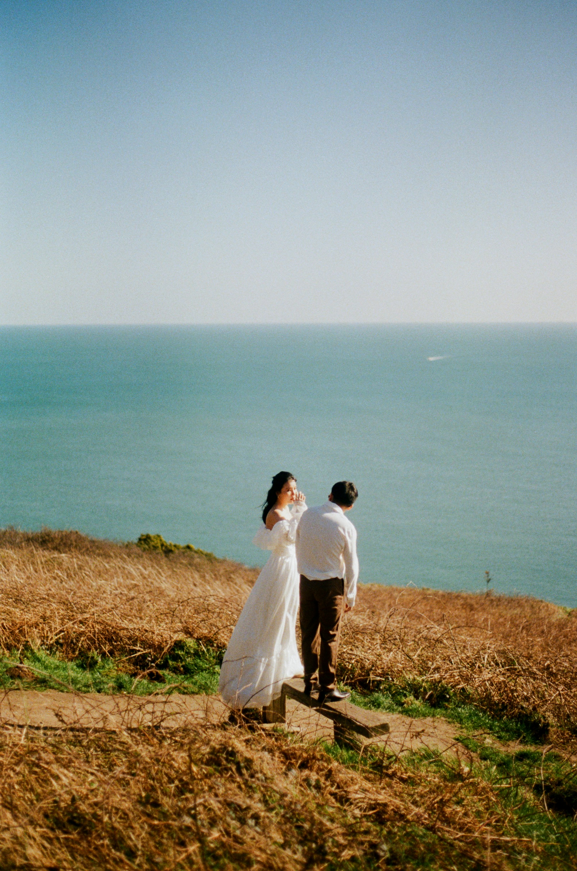 Couple in wedding attire on a cliff overlooking the ocean