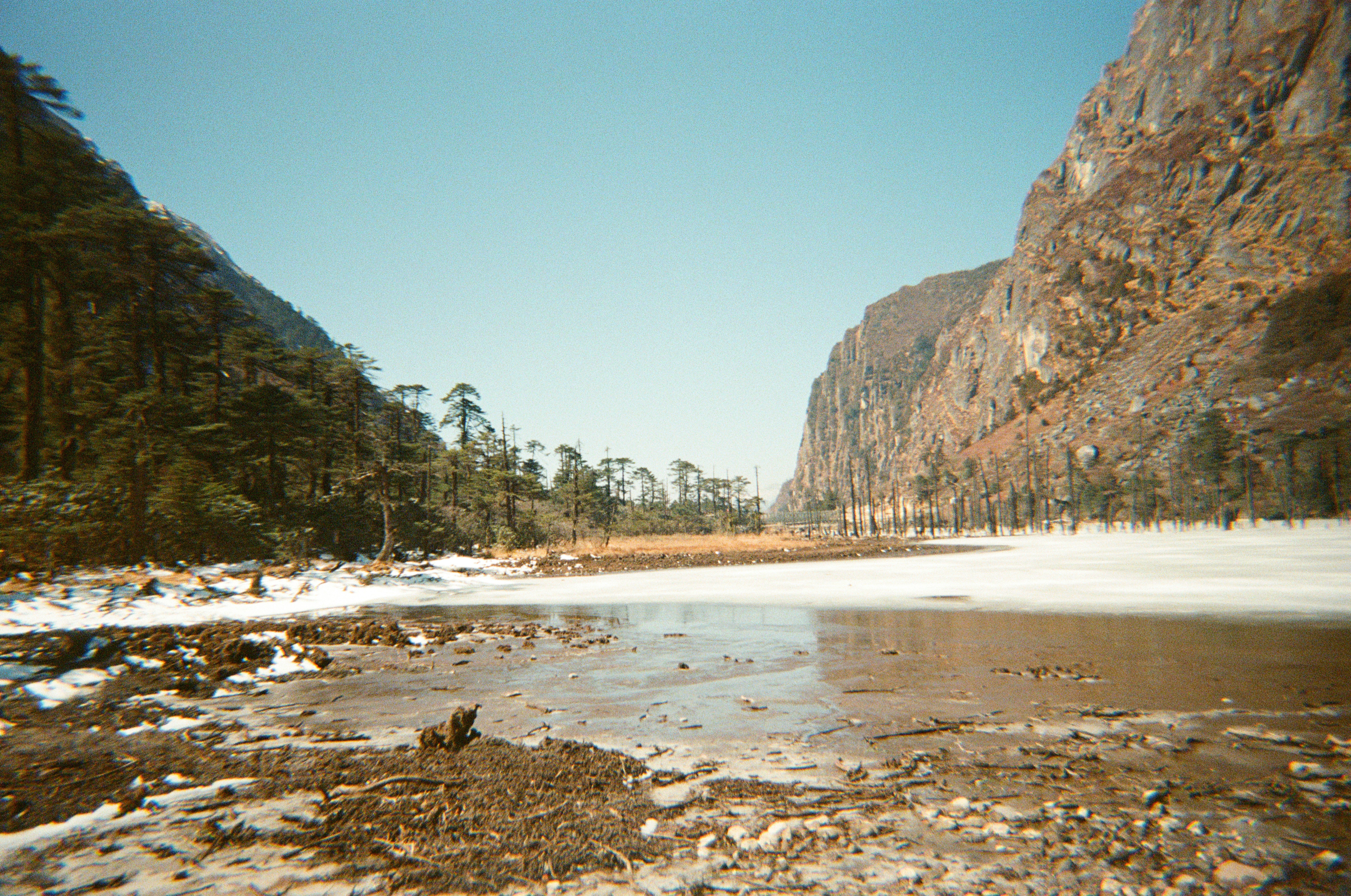 Frozen lake between steep, rocky mountains and pine trees.