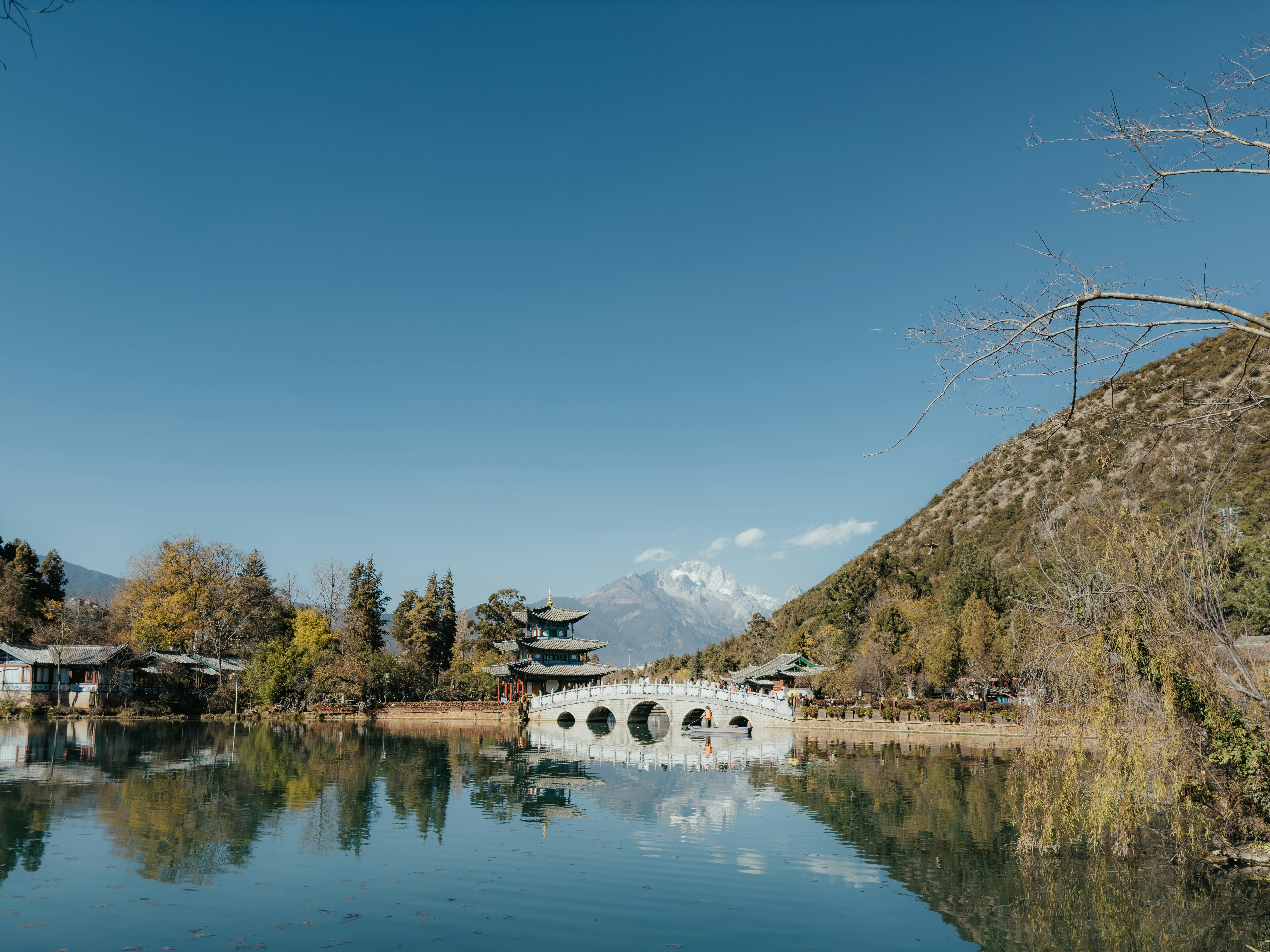 Puente de piedra sobre un lago tranquilo con montañas lejanas.