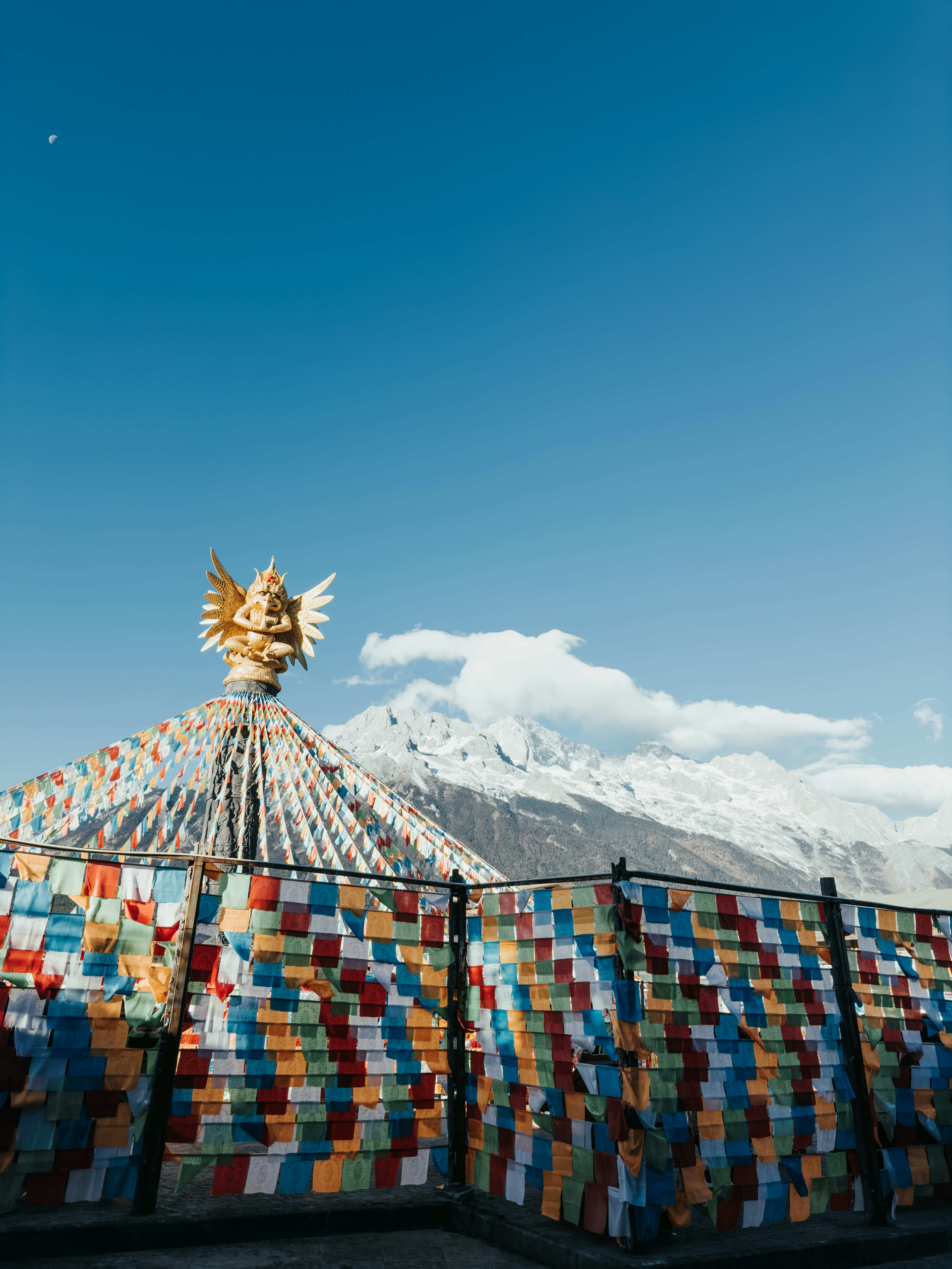 Coloridas banderas de oración adornan una estupa con montañas nevadas detrás.