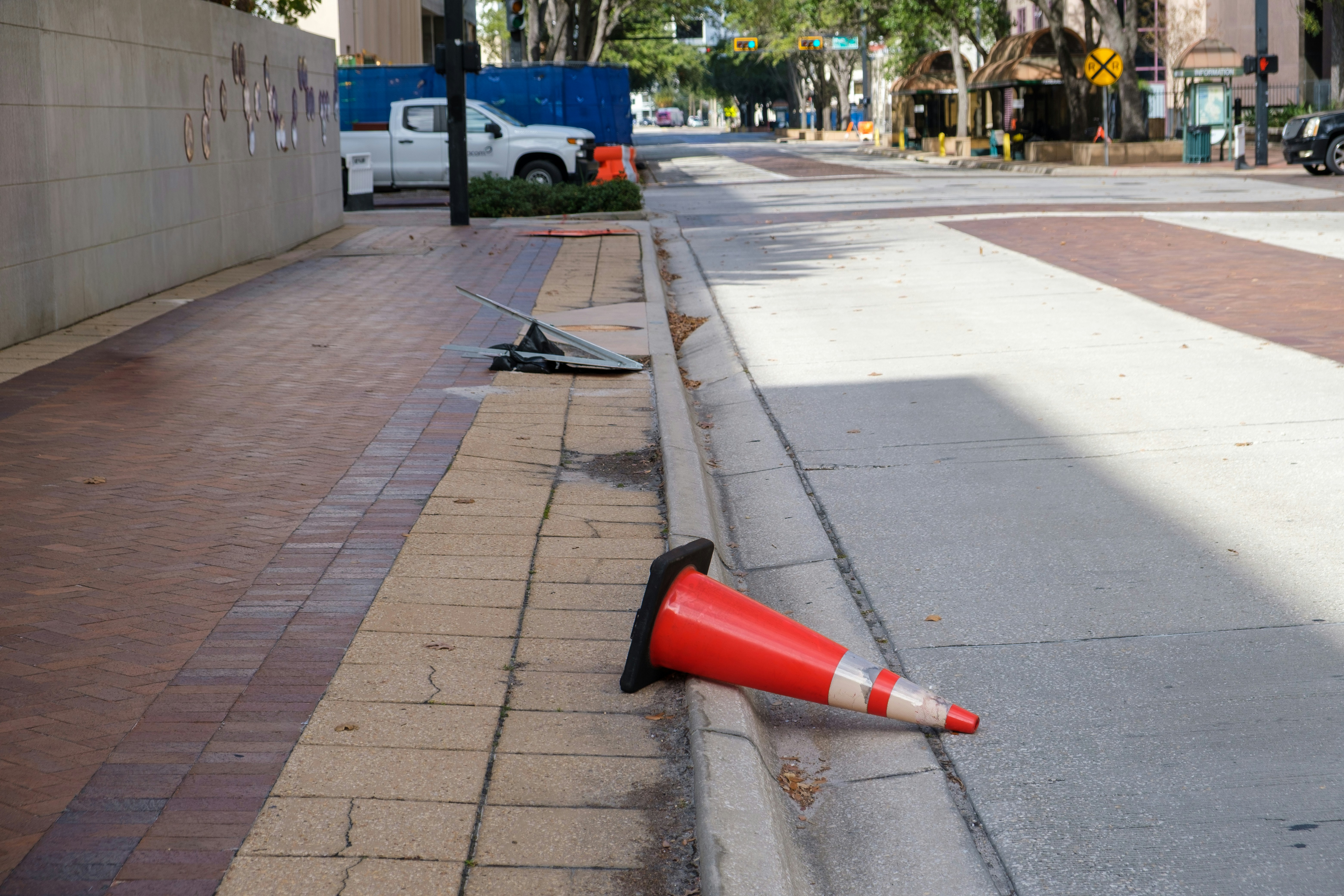 A fallen orange traffic cone lies on the sidewalk.