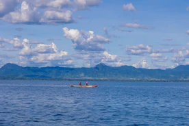 Two people kayak on a calm blue lake near mountains.