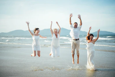 Four people in white jumping on a beach