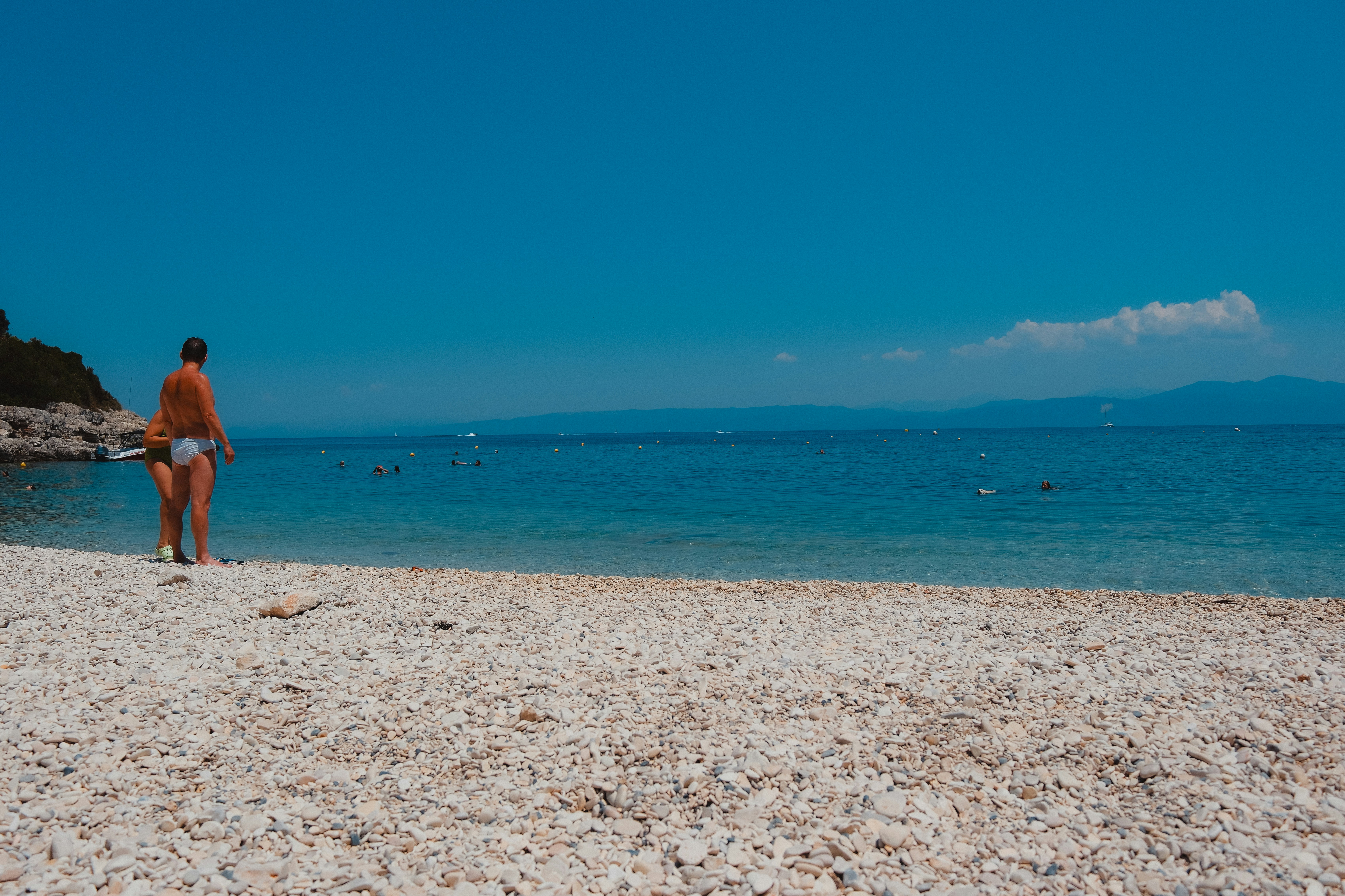 Man walking on a pebble beach towards the ocean.