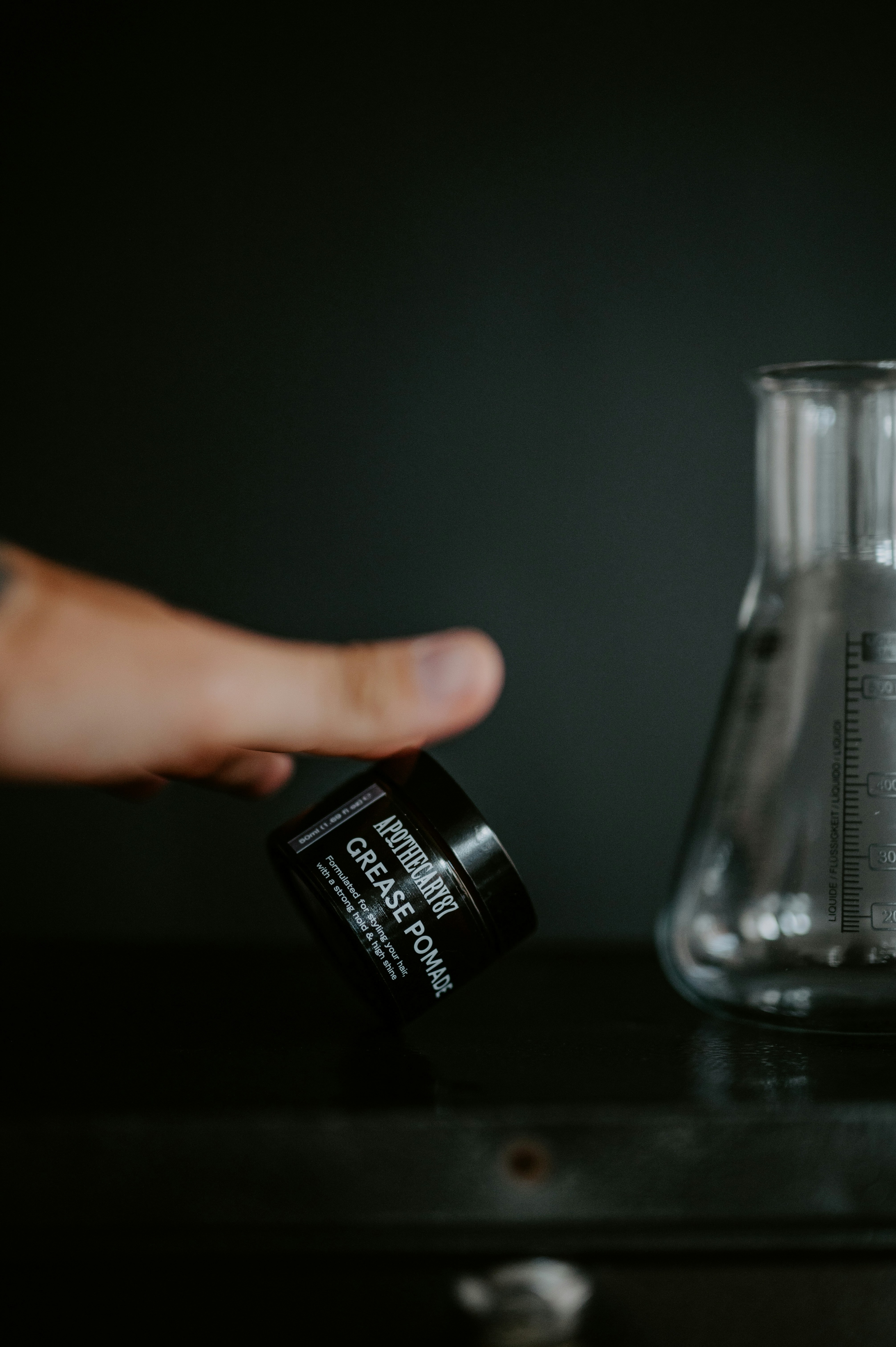Hand hält ein Glas Fettpomade in der Nähe der Flasche