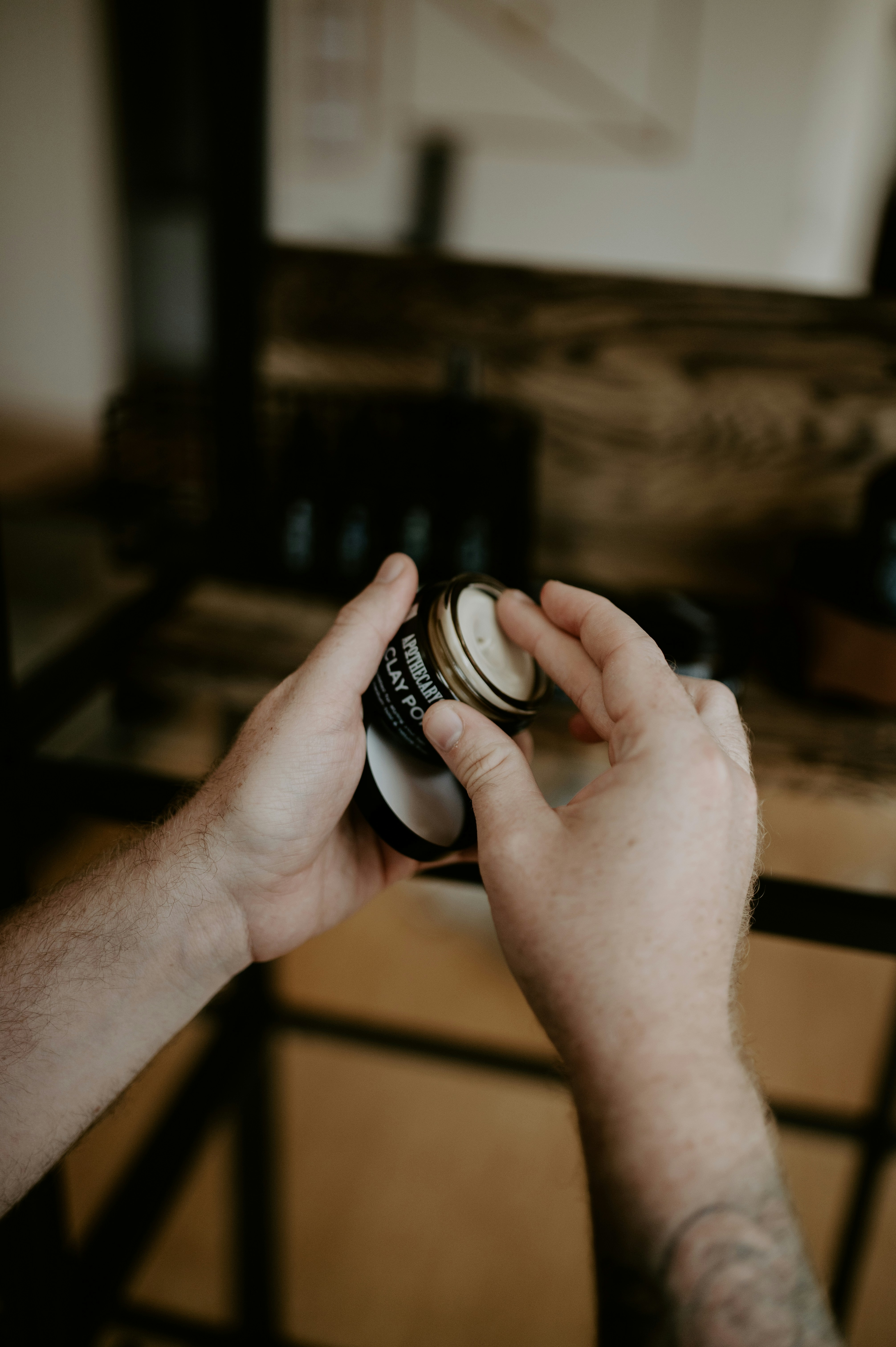 Hands opening a small container of hair product.