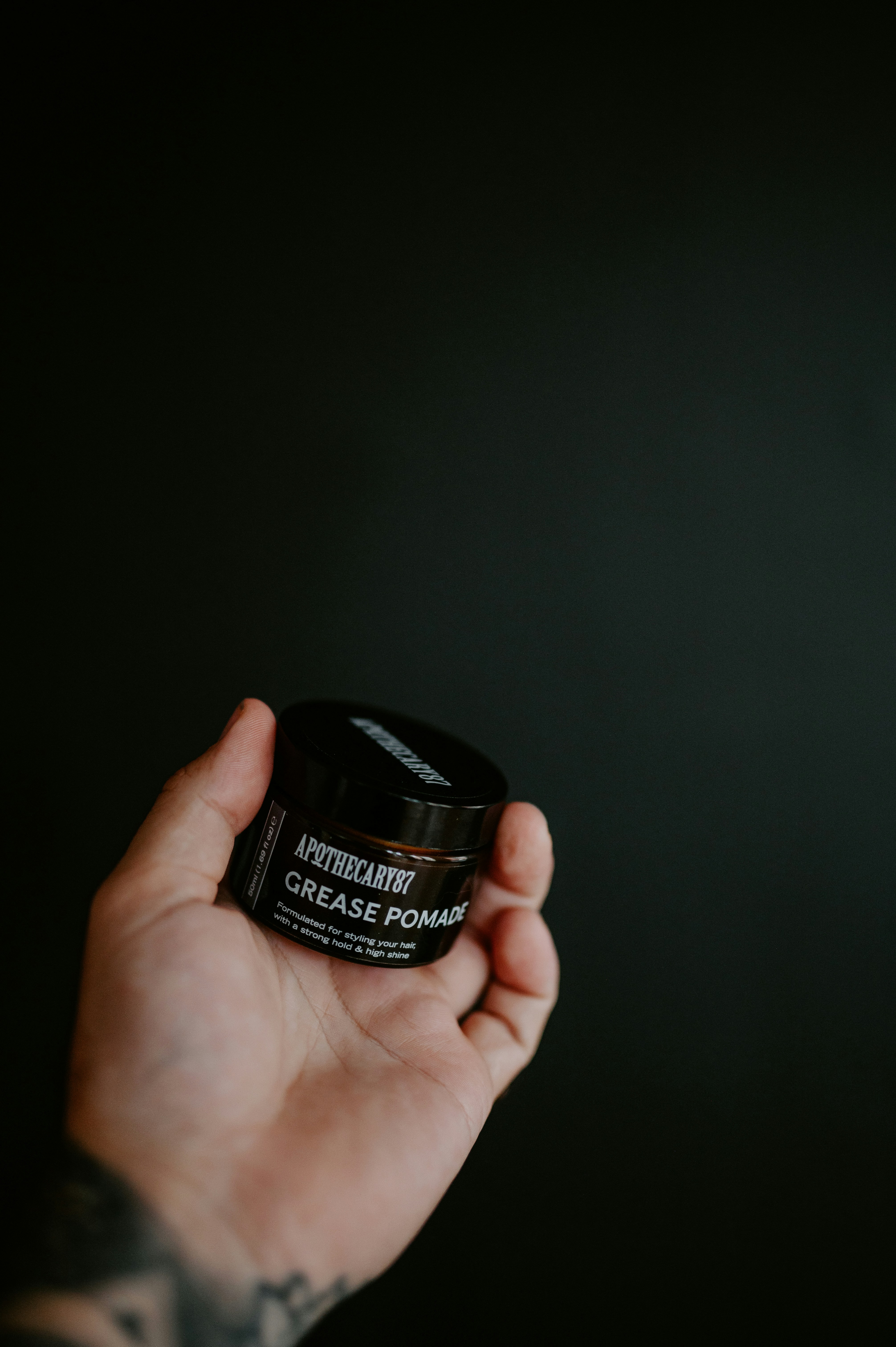 Hand holding a jar of grease pomade