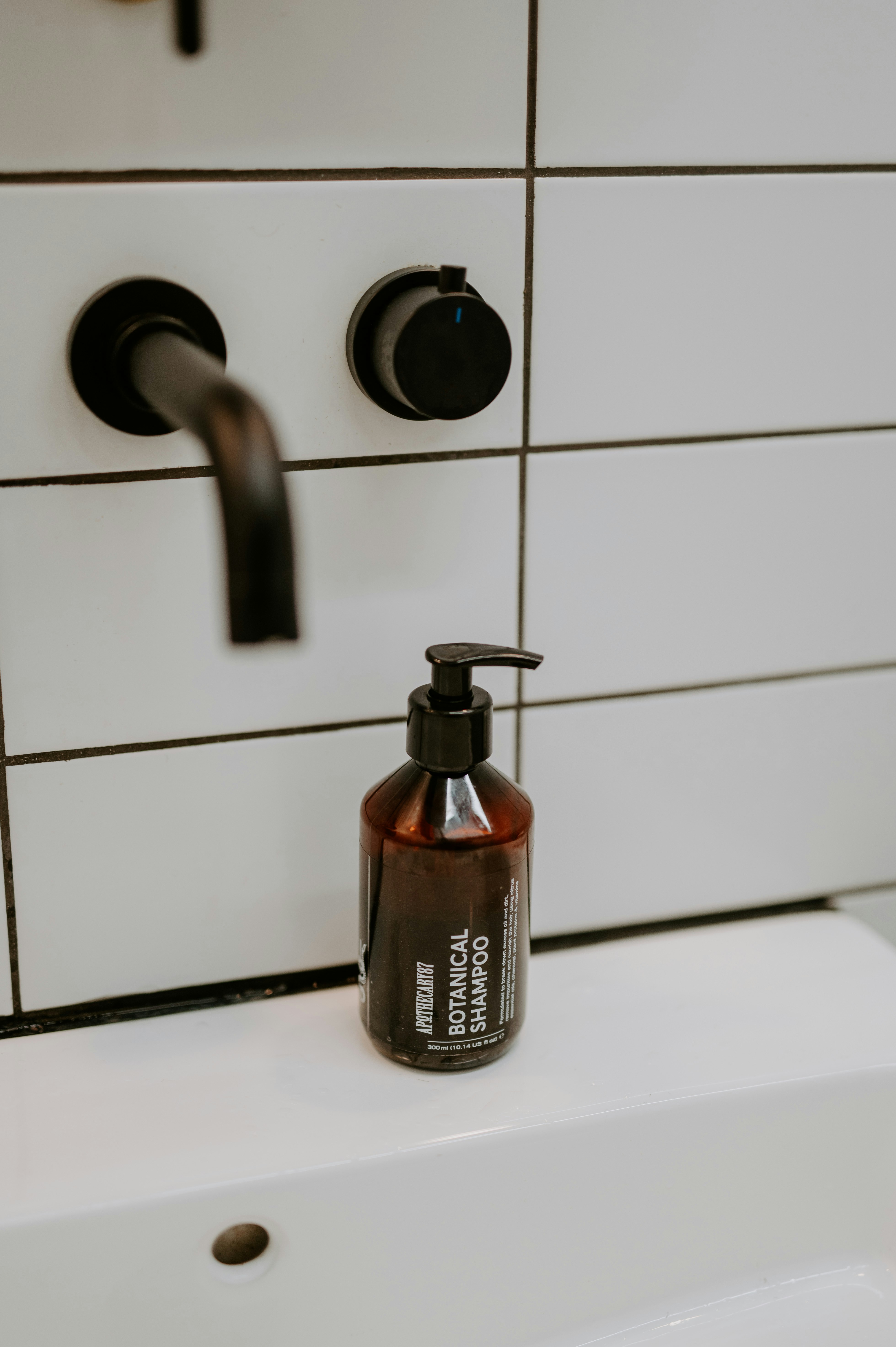 A dark bottle of botanical shampoo sits on a sink.