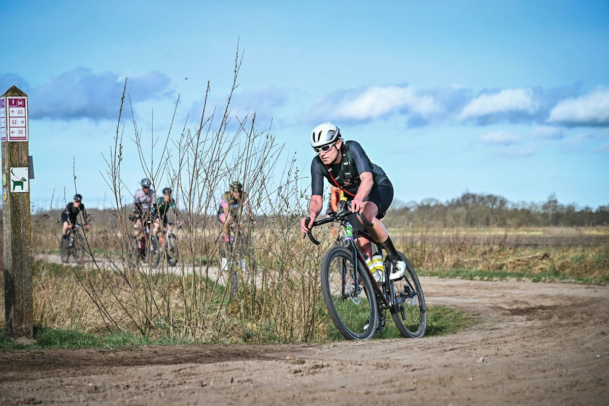 Cyclistes de gravel en course sur un chemin de terre, sous un ciel bleu