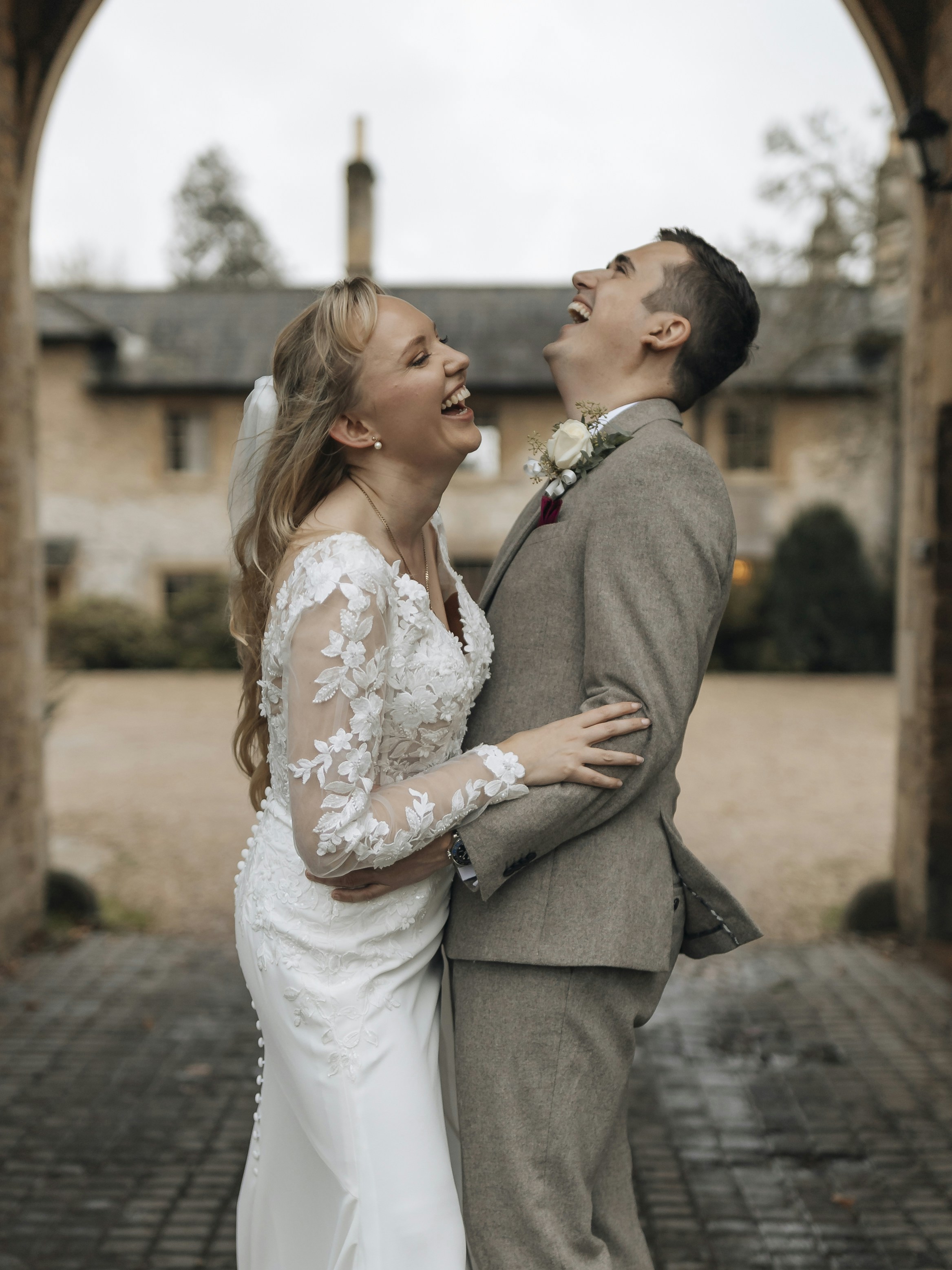 A laughing bride and groom embrace under an archway.