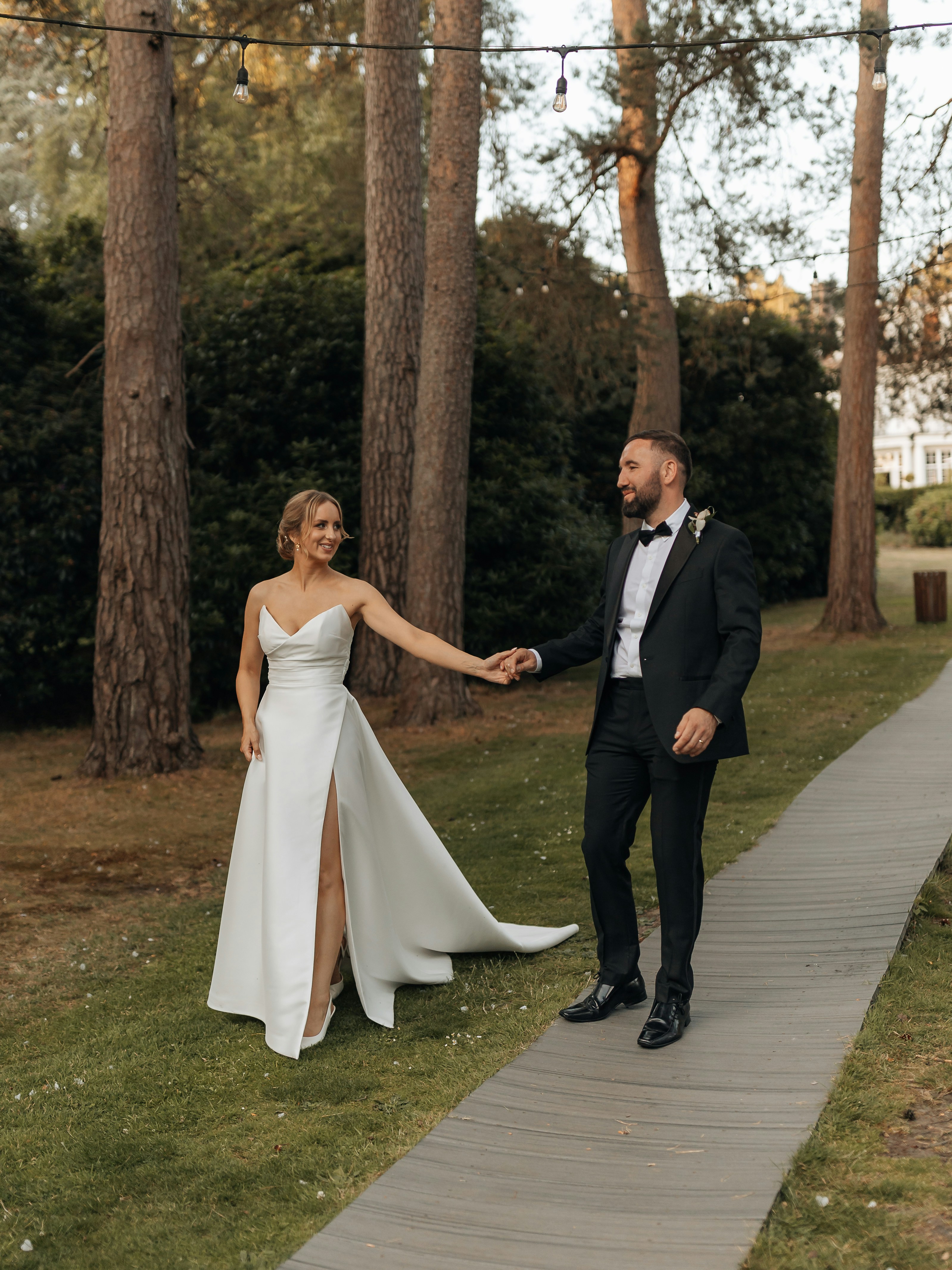 A bride and groom walking hand in hand outdoors.