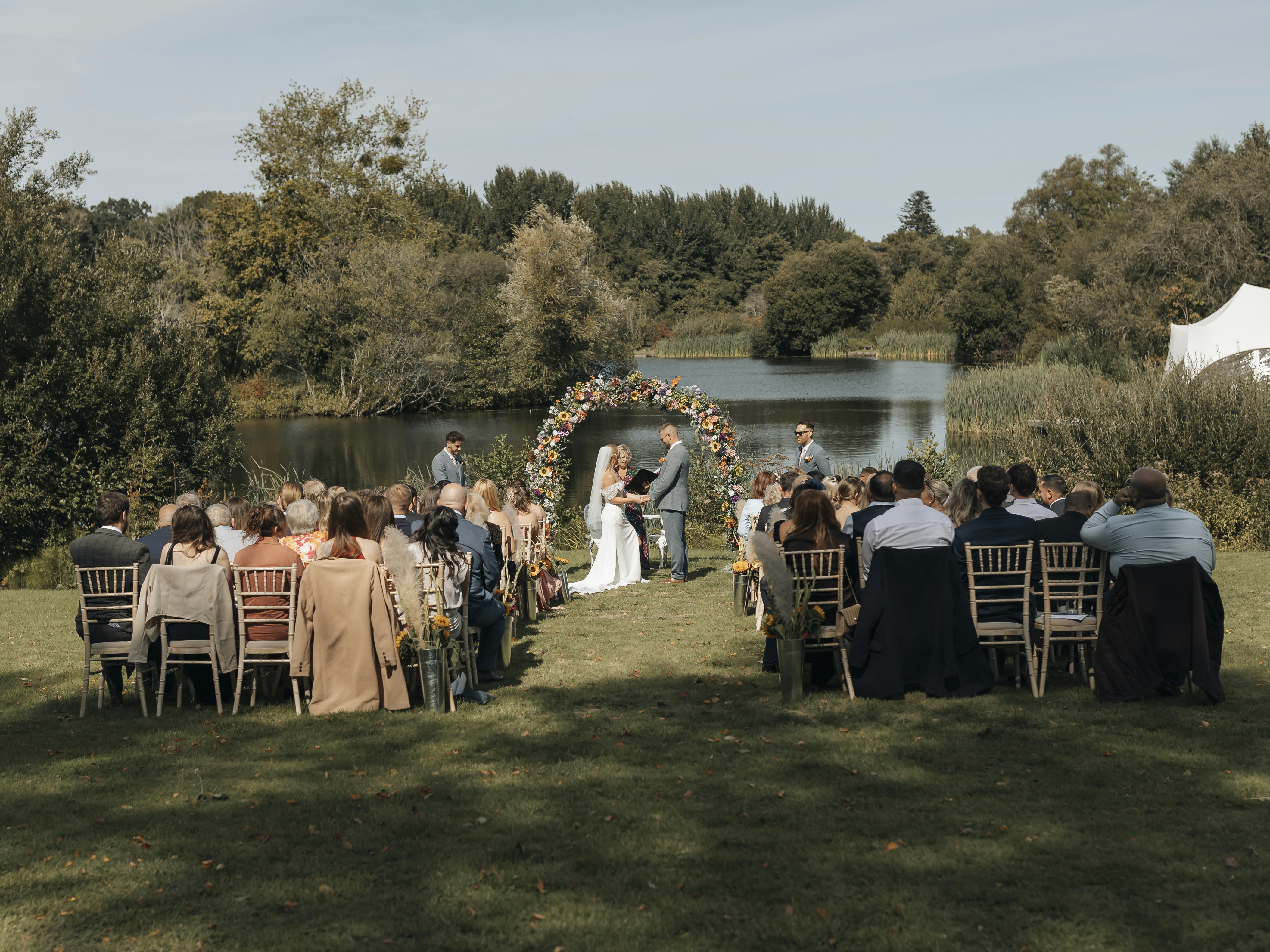 Wedding ceremony by a lake with guests seated outdoors.