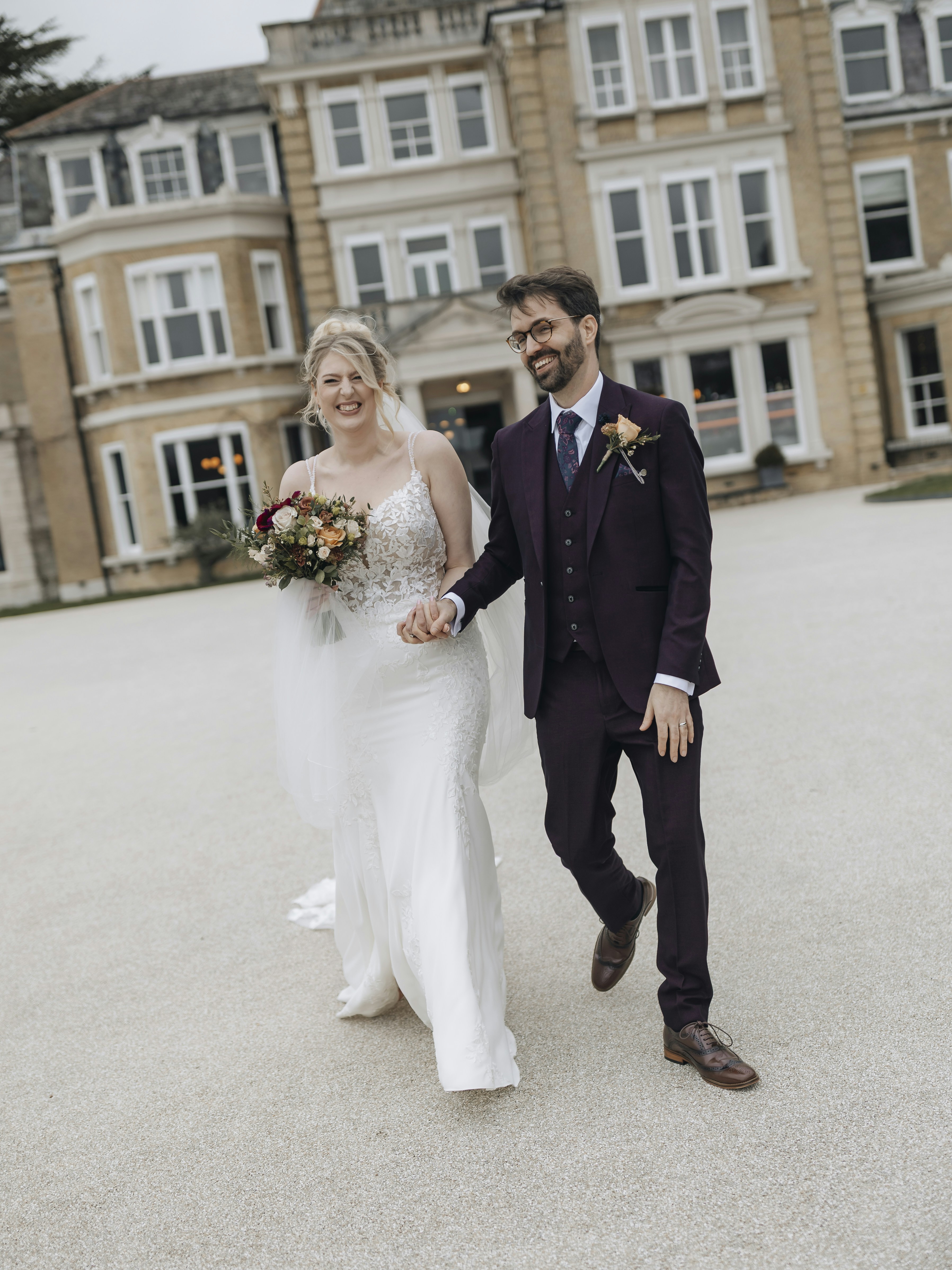 A bride and groom walk hand-in-hand outside a building.