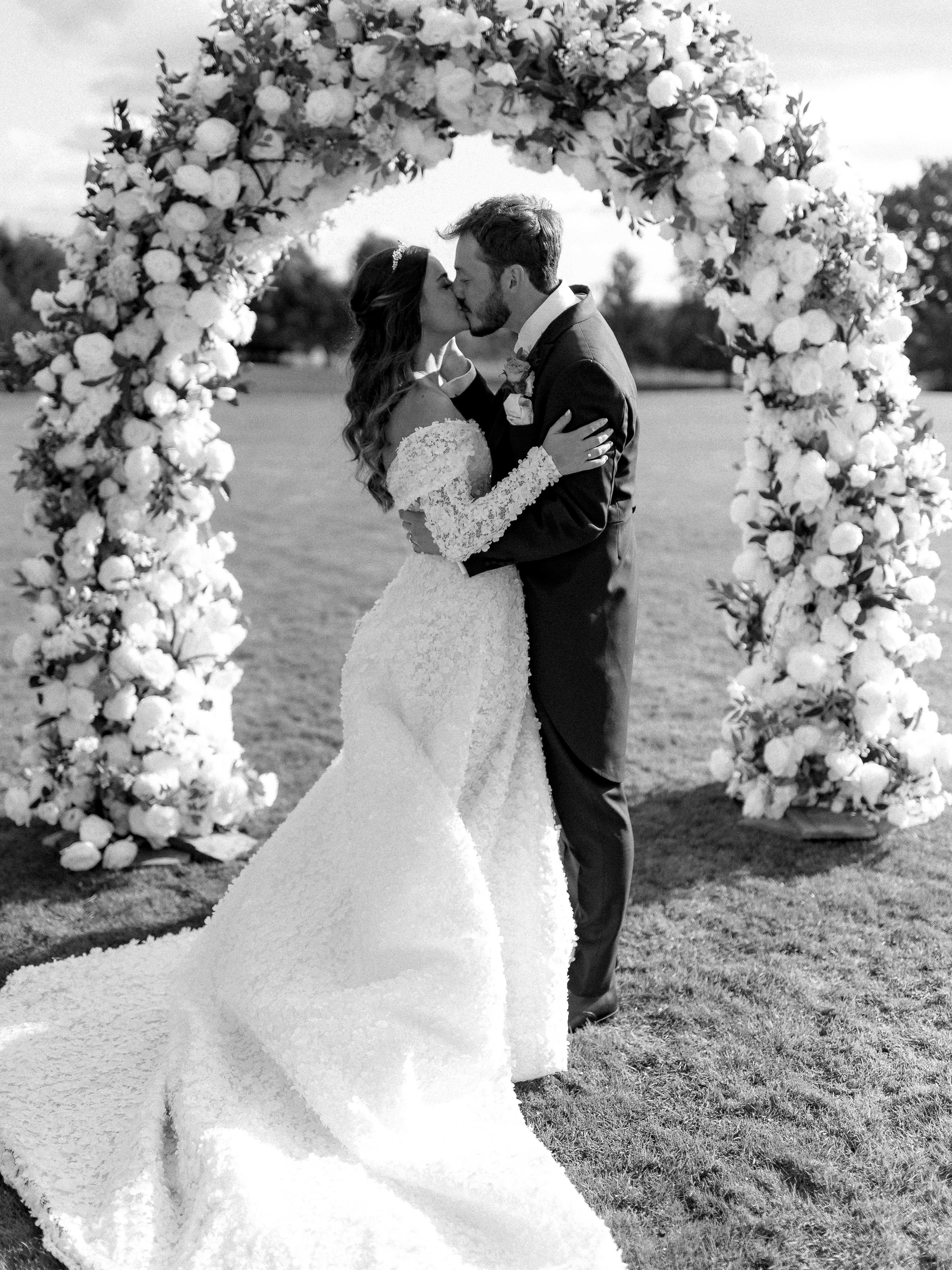 Bride and groom kissing under floral wedding arch.