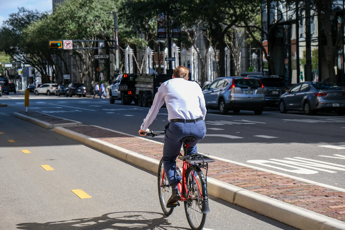 Pessoa a pedalar numa ciclovia protegida, no meio do trânsito urbano